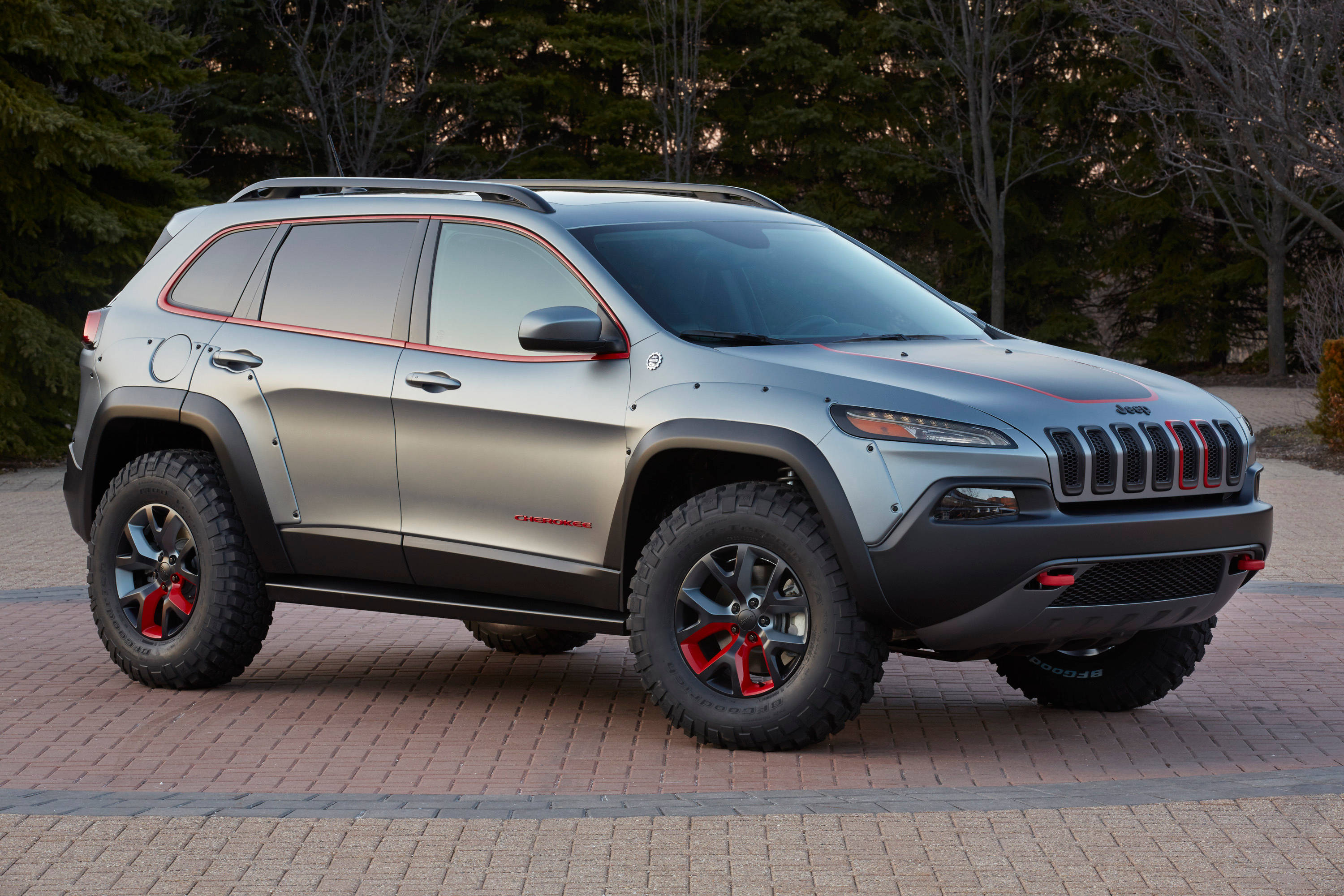 吉普 桌布 壁紙 — 一輛銀色Jeep Cherokee，帶有紅色點綴和堅固輪胎，停在磚砌車道上，周圍樹木環繞。