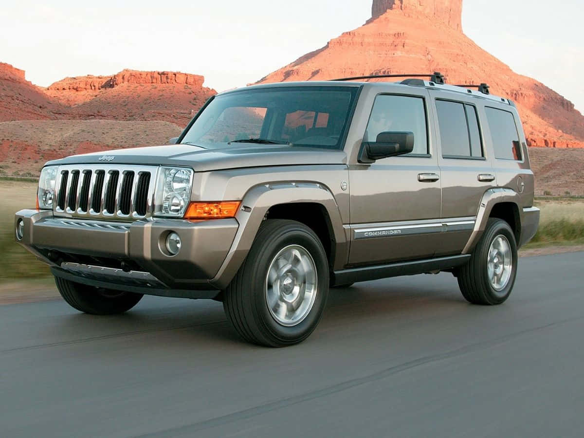 Jeep Commander 桌布 壁紙 — 一輛銀色Jeep Commander SUV在沙漠公路上行駛，背景是日落時分的紅色岩層。