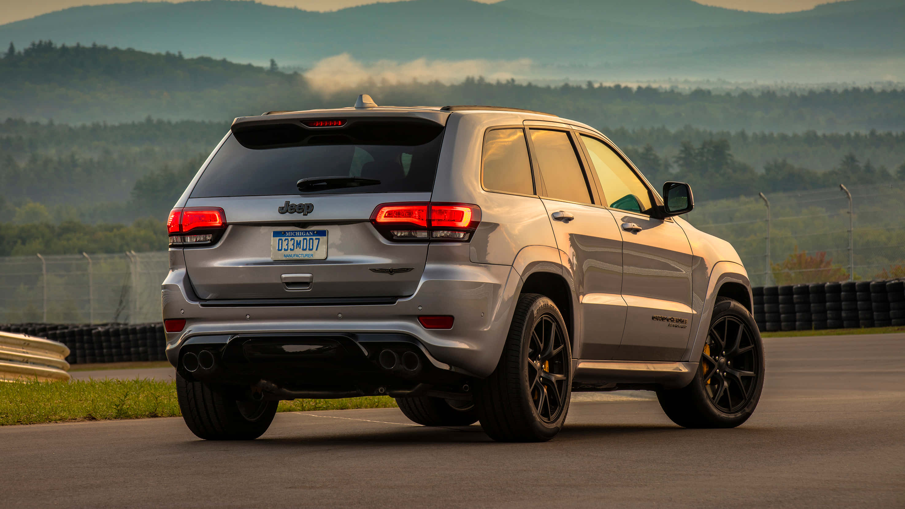 Jeep Trackhawk 桌布 壁紙 — 一輛銀色Jeep Grand Cherokee Trackhawk在日出時停泊在賽道上，背景是霧氣瀰漫的山巒。