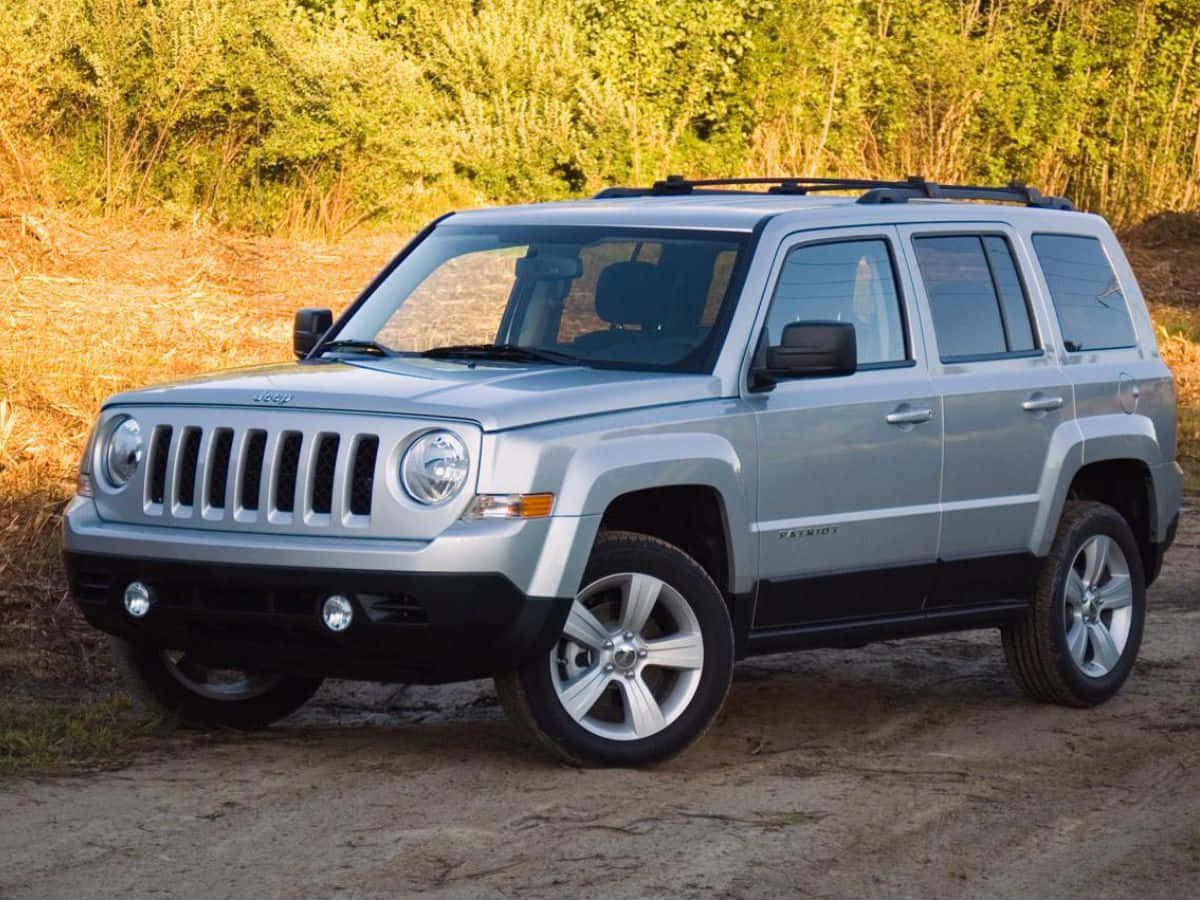 Jeep Patriot 桌布 壁紙 — 一輛銀色Jeep Patriot SUV停放在泥土小徑上，背景有金色樹葉和綠色灌木。