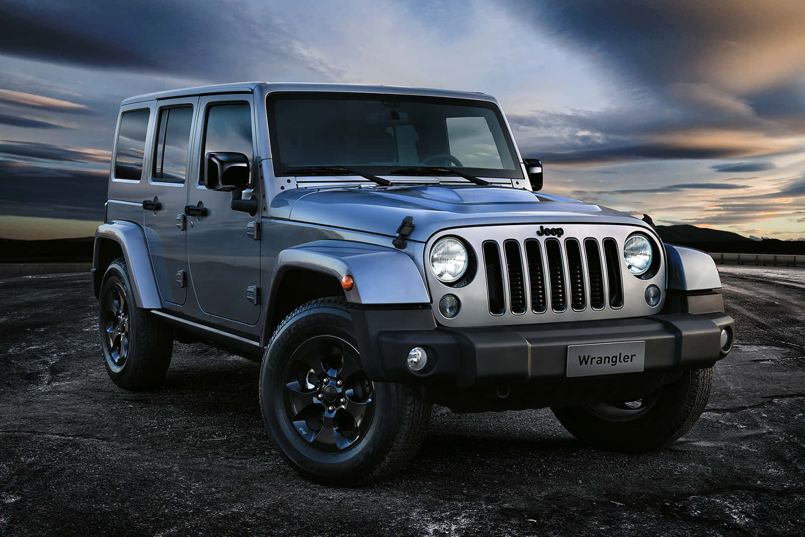 黑色吉普車 桌布 壁紙 — 一輛銀色Jeep Wrangler在裂開的瀝青上堅固地停放，背景是帶有條紋雲的戲劇性黃昏天空。