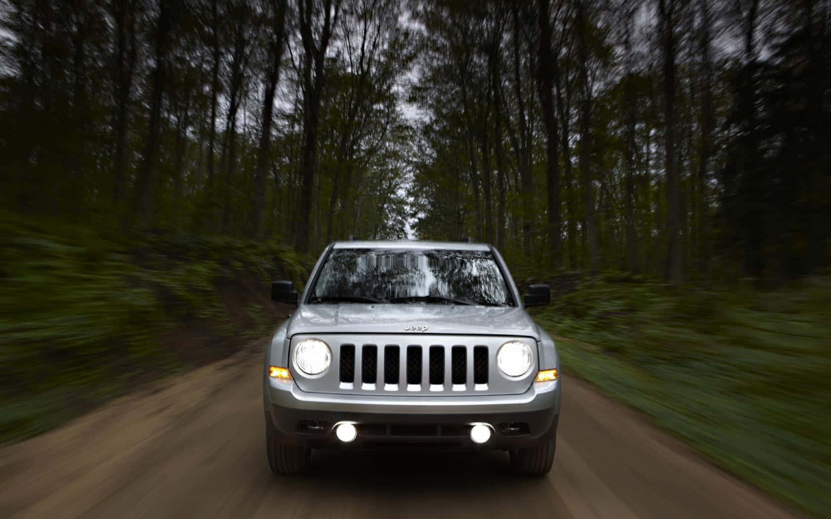 Jeep Patriot 桌布 壁紙 — 一輛銀色Jeep Wrangler在陰天下一條森林道路上疾馳，模糊的樹木飛掠而過。