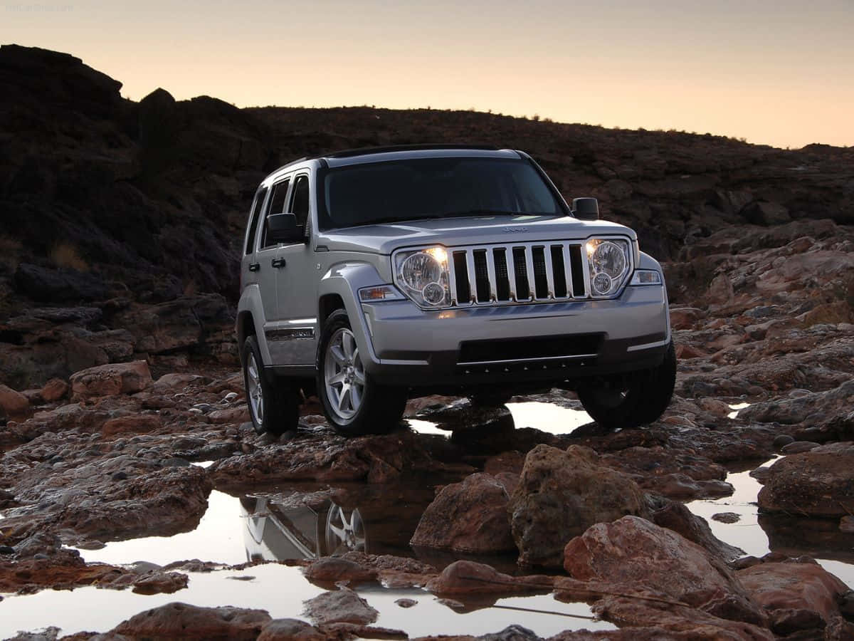 Jeep Liberty 桌布 壁紙 — 一輛銀色Jeep Wrangler在日落時分穿越岩石地形，水坑反射其車頭燈。