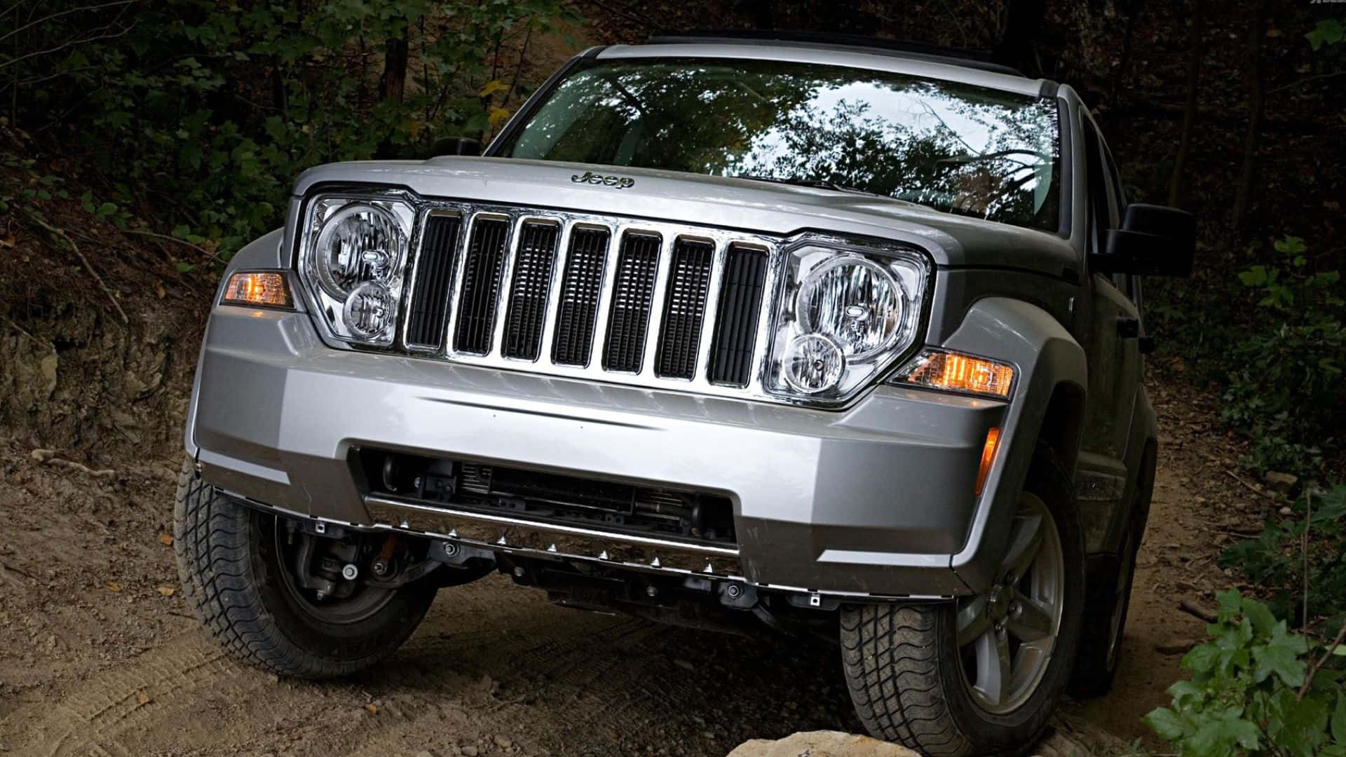 Jeep Liberty 桌布 壁紙 — 一輛銀色Jeep Wrangler在茂密的森林中行駛在崎嶇的泥土路上，斑駁的陽光穿過樹木灑落。