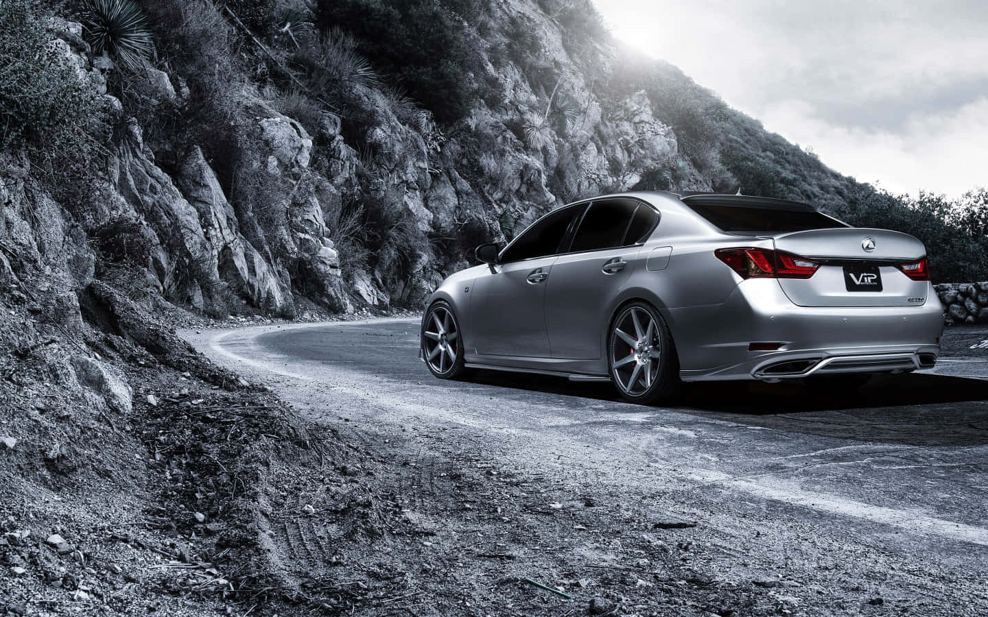 Lexus Gs 桌布 壁紙 — 一輛銀色Lexus轎車在陰天下行駛於蜿蜒的山路，兩旁是崎嶇的懸崖和稀疏的植被。
