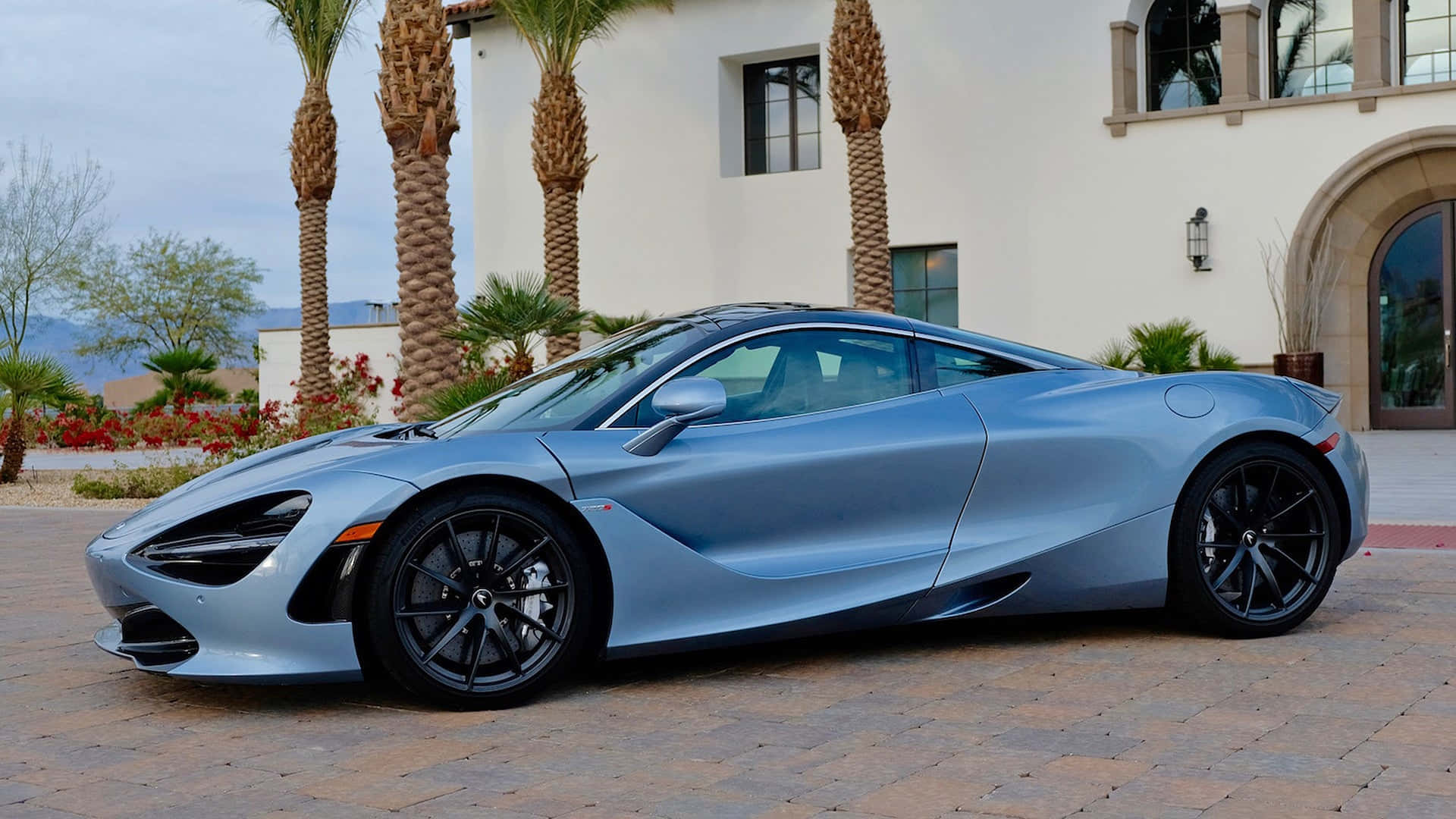 麥拉倫 桌布 壁紙 — 一輛銀色McLaren 720S跑車停放在石頭車道上，前面是帶有棕櫚樹的灰泥豪宅。