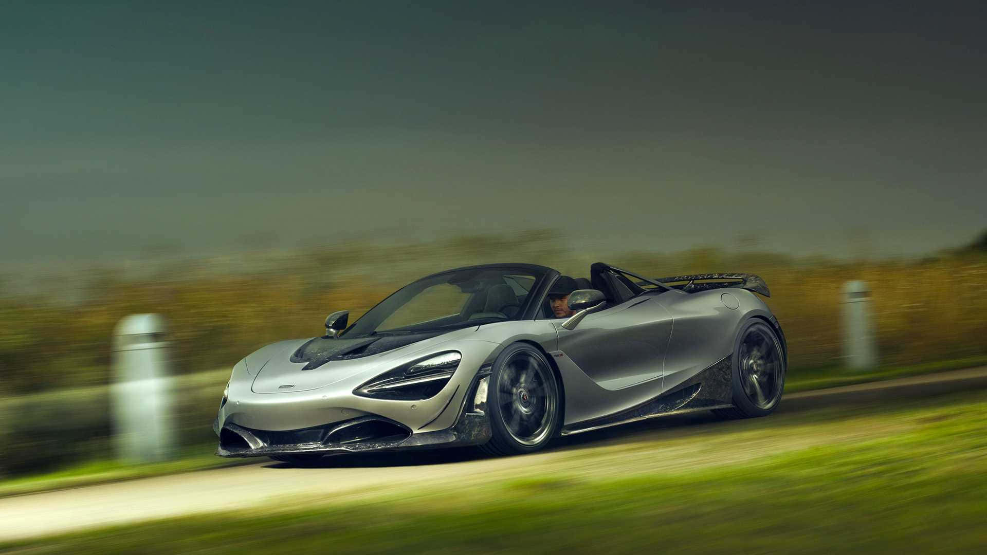 Gray Aesthetic 桌布 壁紙 — 一輛銀色McLaren 720S Spider在蜿蜒的道路上疾馳，背景是模糊的綠色植物和白色柱子。