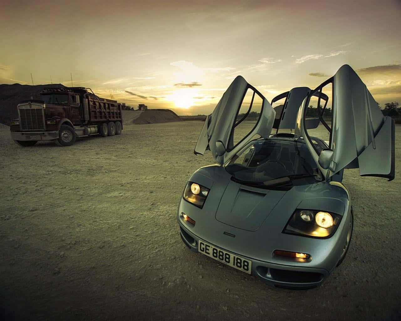 跑車 桌布 壁紙 — 一輛銀色McLaren F1打開鷗翼車門，在日落時分停泊在塵土飛揚的沙漠中，旁邊是一輛大型紅色自卸卡車。