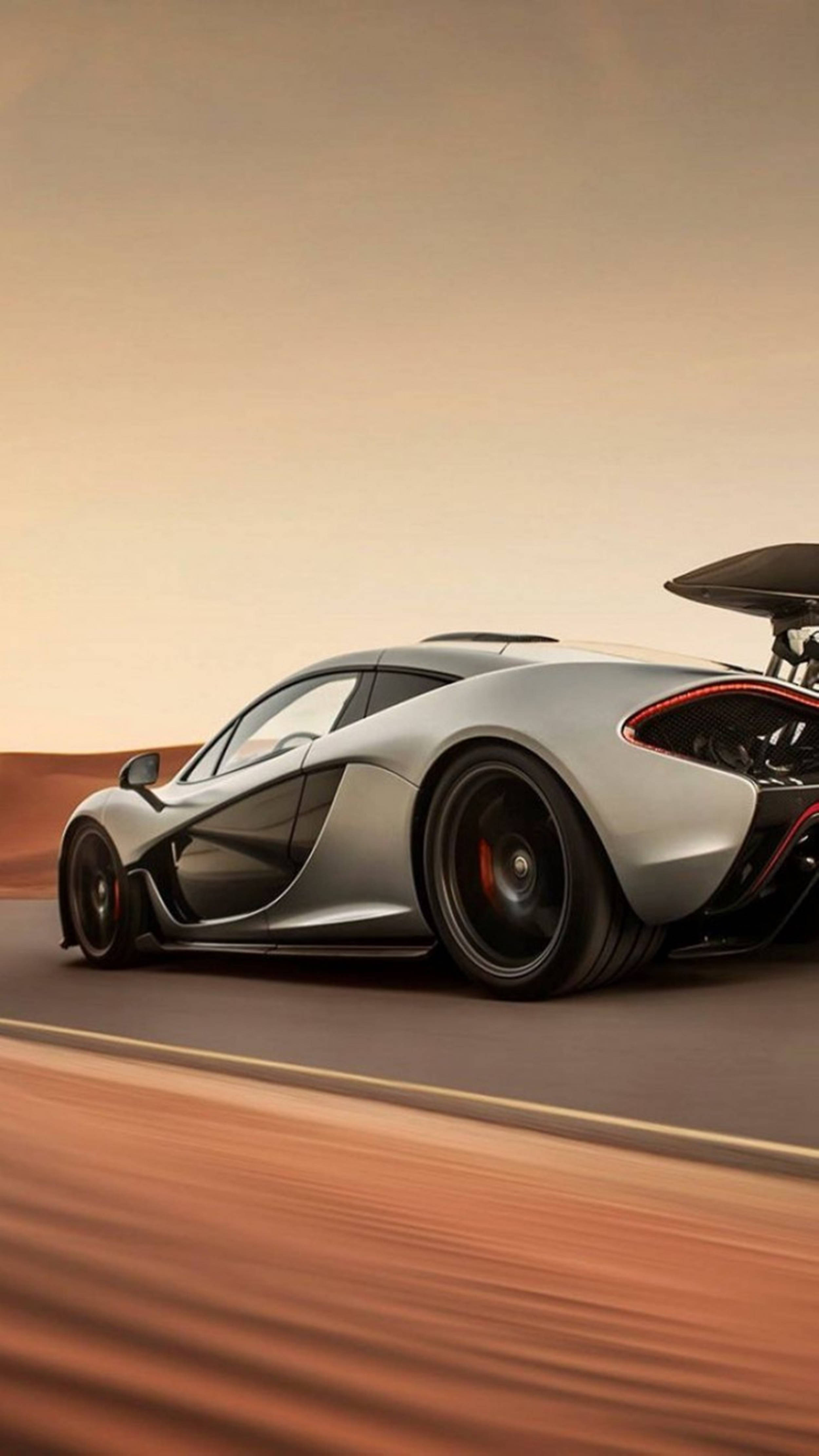 Luxury 桌布 壁紙 — 一輛銀色McLaren P1超級跑車在溫暖的橙色天空下，沿著沙漠公路疾馳，帶有動態模糊效果。