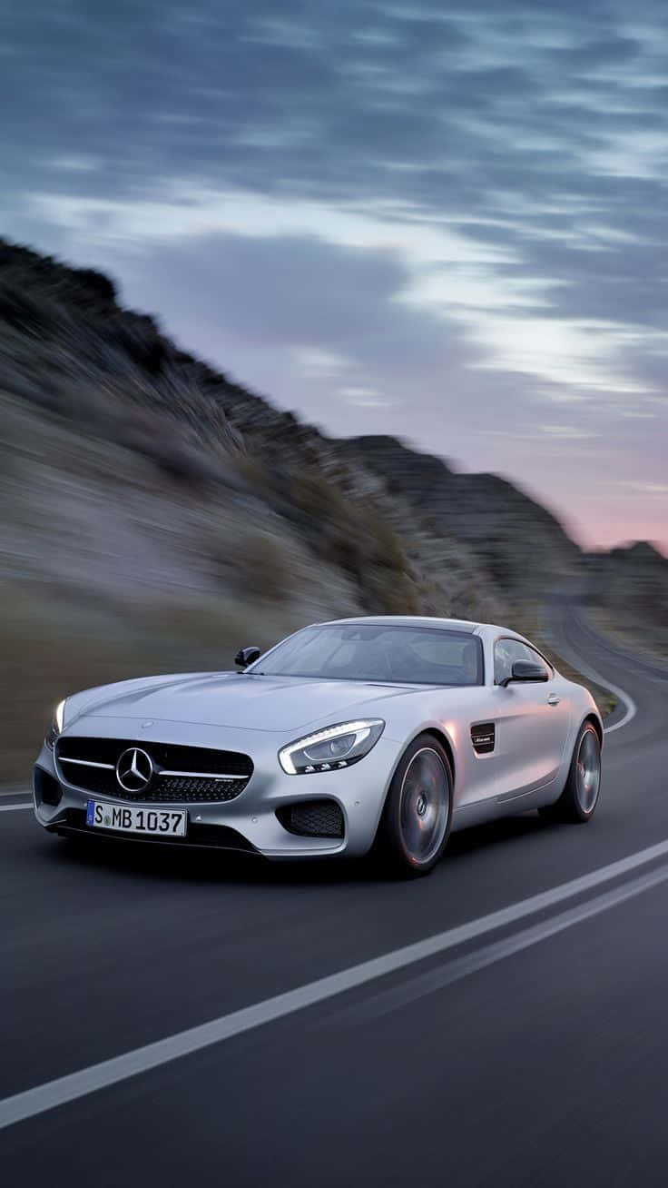 Mercedes 桌布 壁紙 — 一輛銀色Mercedes-AMG GT在黃昏時分沿著蜿蜒的山路疾馳，背景是模糊的岩石地形。