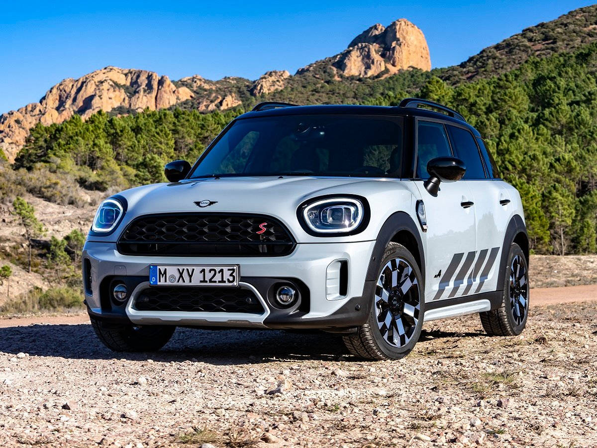 Mini 桌布 壁紙 — 一輛銀色MINI Countryman S大膽地停在陽光明媚的碎石路上，背景是崎嶇的山脈和綠樹。