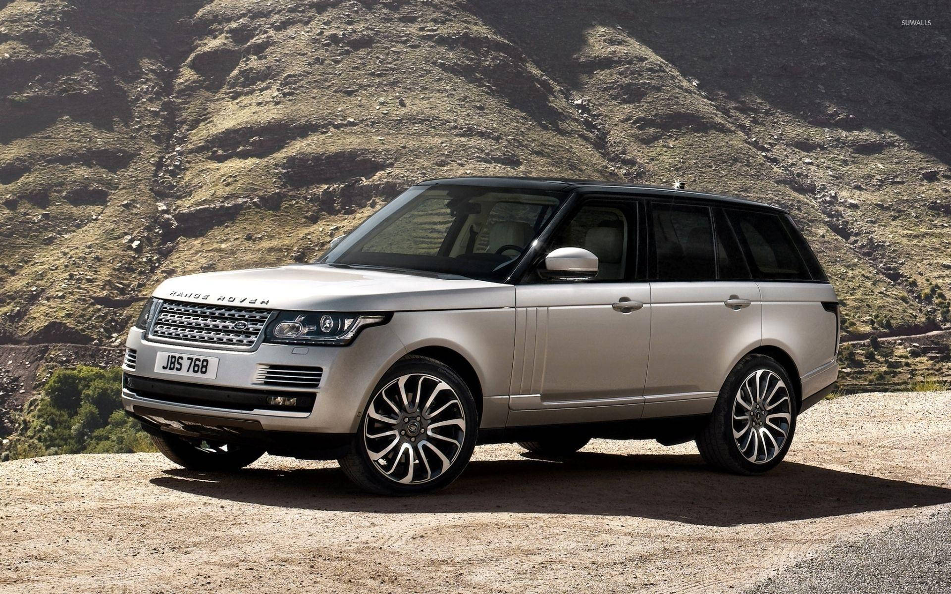 4K 桌布 壁紙 — 一輛銀色Range Rover SUV停泊在塵土飛揚的山路上，背景是崎嶇的山丘。