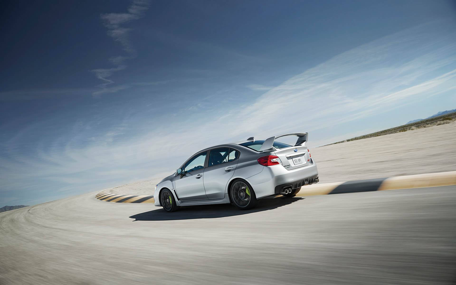 昴 桌布 壁紙 — 一輛銀色Subaru WRX STI在晴朗藍天下，以動態模糊效果在沙漠賽道上奔馳。