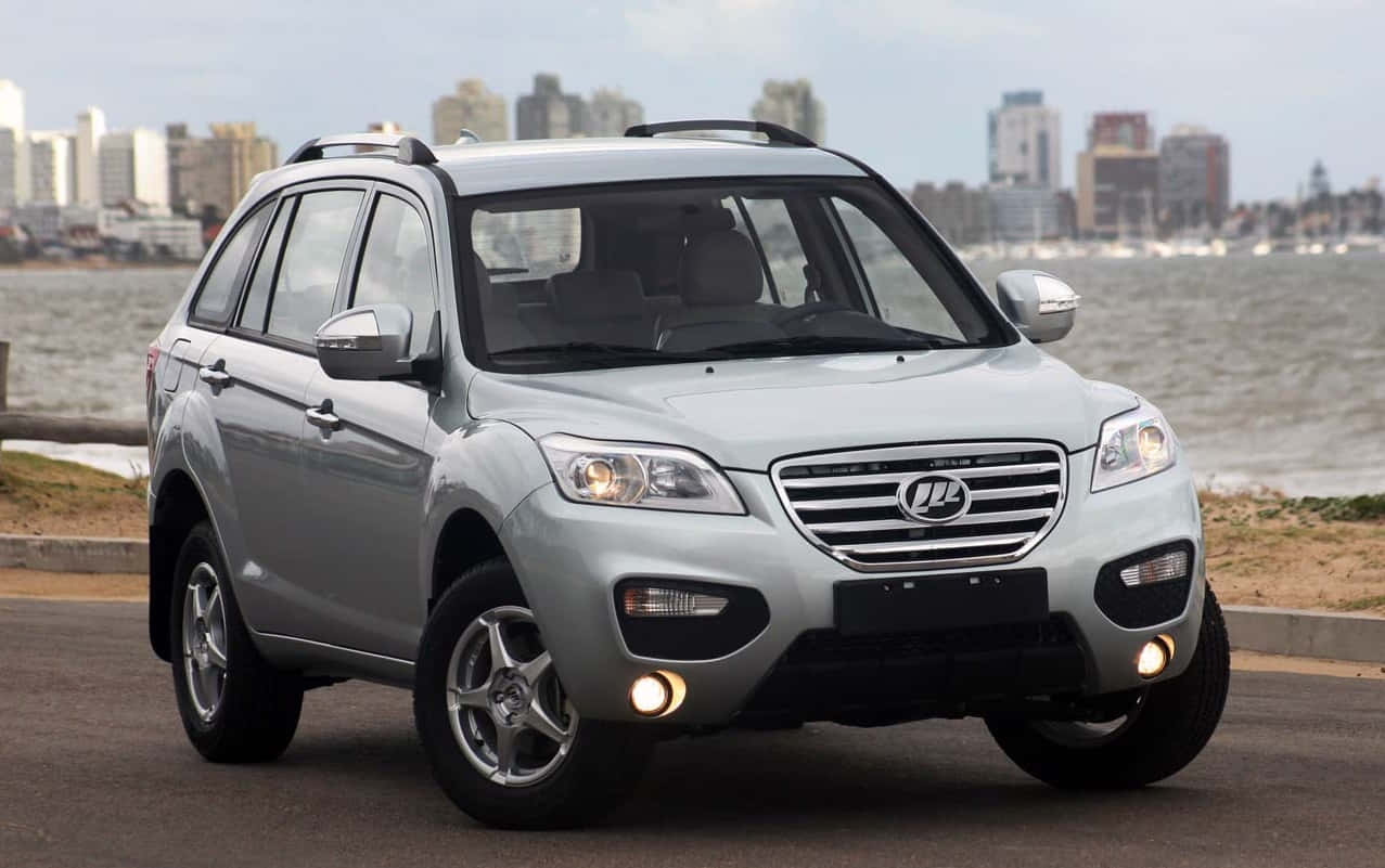 Lifan 桌布 壁紙 — 一輛銀色SUV停泊在海濱道路上，背景是城市天際線和水。