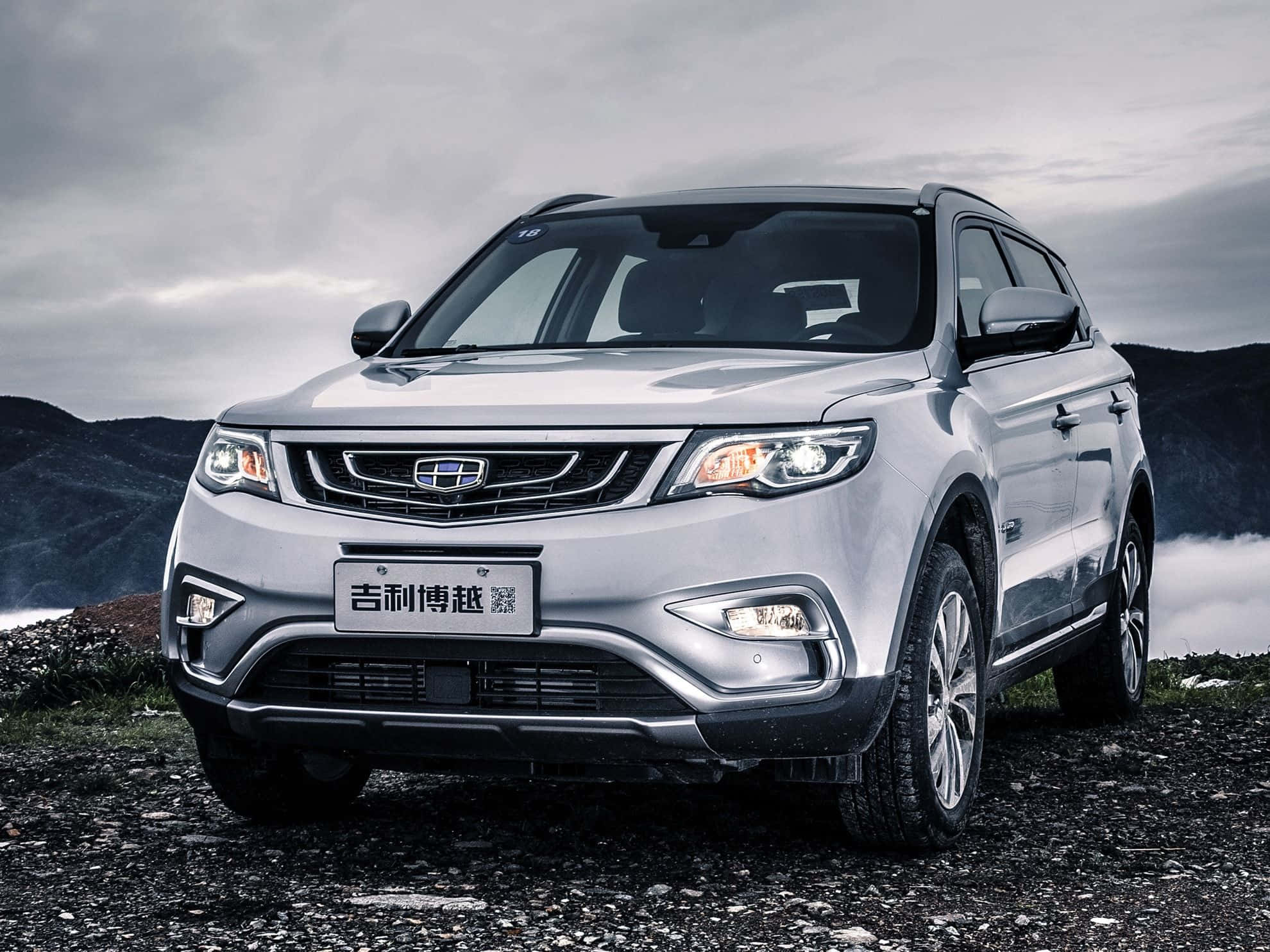 Geely 桌布 壁紙 — 一輛銀色SUV在岩石山坡上蓄勢待發，天空多雲，背景有遠山。