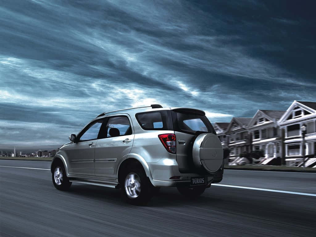 Daihatsu 桌布 壁紙 — 一輛銀色SUV在戲劇性的多雲天空下高速行駛在高速公路上，路邊排列著郊區房屋。