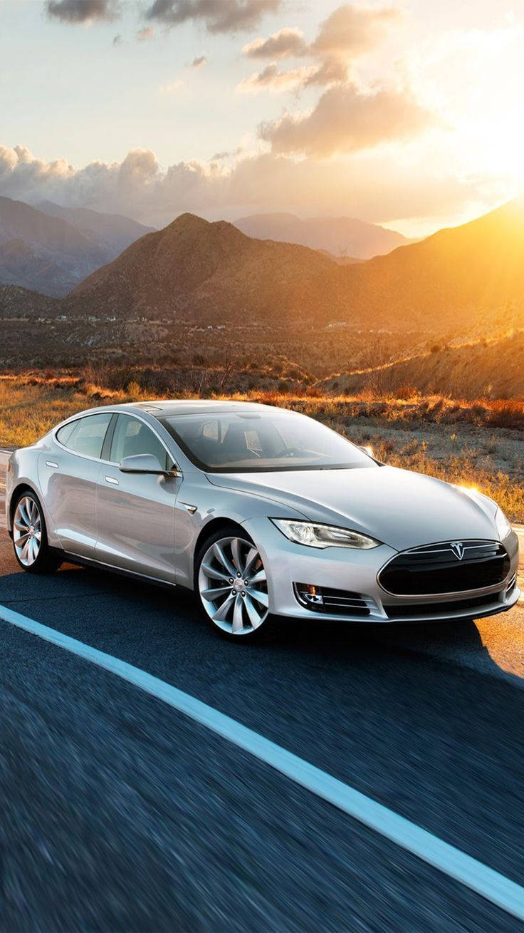 特斯拉 桌布 壁紙 — 一輛銀色Tesla Model S在日落時分沿沙漠公路飛馳，背景是金色的山脈。