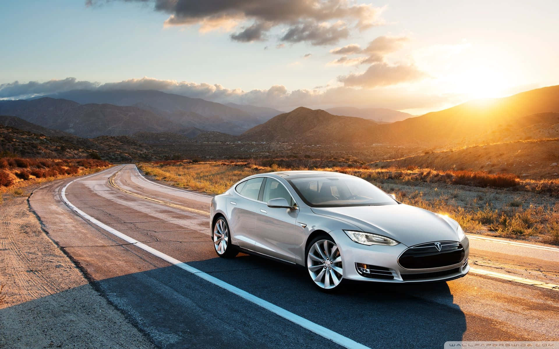 Hybrid Car 桌布 壁紙 — 一輛銀色Tesla Model S沿著蜿蜒的山路行駛，沐浴在金色的夕陽光中。