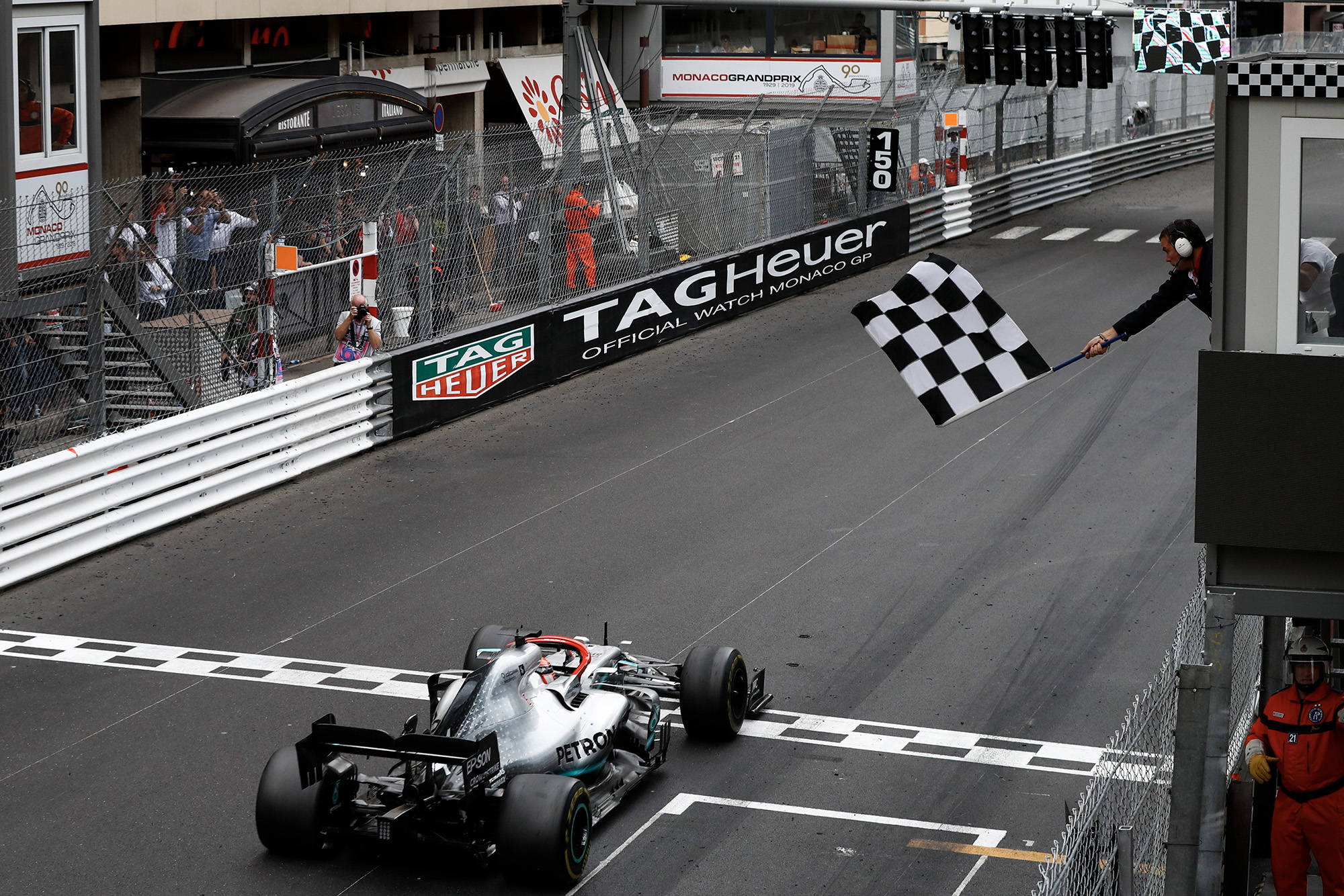 Checkered Flag 桌布 壁紙 — 一輛銀色一級方程式賽車在摩納哥大獎賽中越過終點線，同時一名賽事工作人員揮舞著方格旗。
