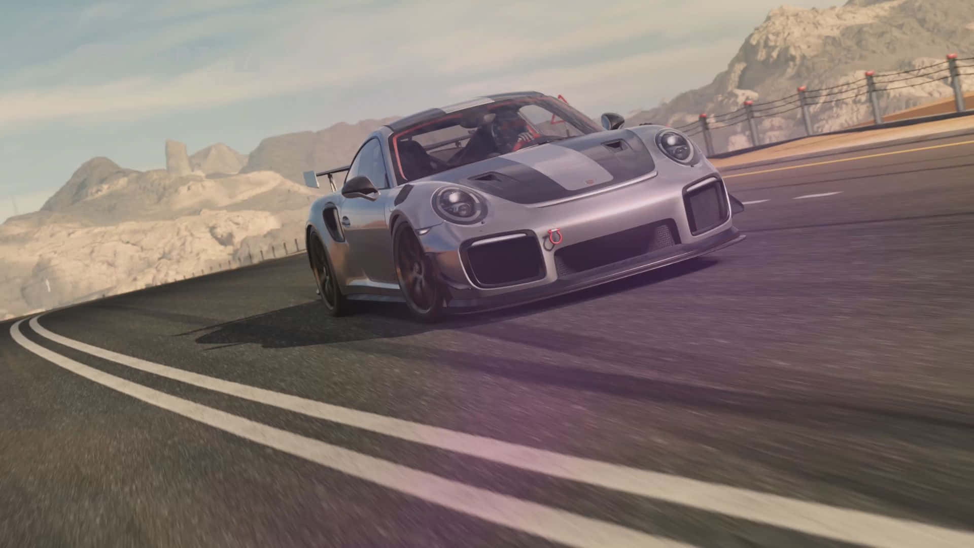 電玩遊戲 桌布 壁紙 — 一輛銀色保時捷 911 GT2 RS 在蜿蜒的山路上疾駛，背景是岩石山峰。