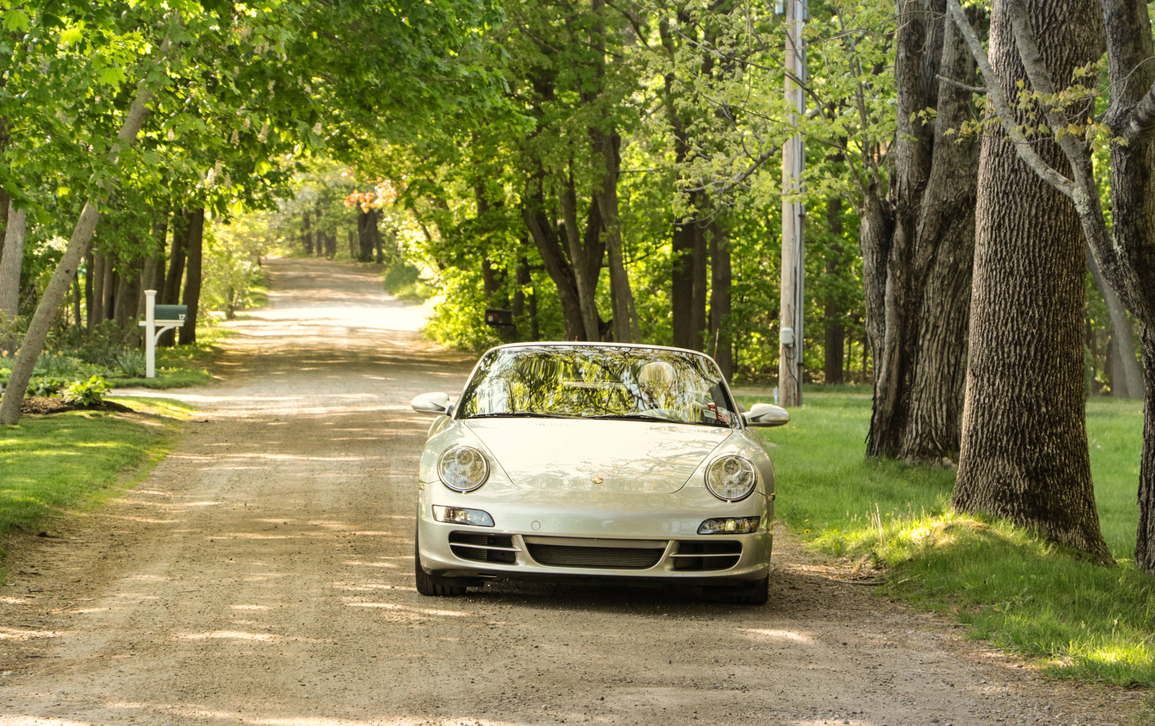 Luxury 桌布 壁紙 — 一輛銀色保時捷 Boxster 敞篷車在夏季停放在一條陽光斑駁、樹木成蔭的泥土路上。