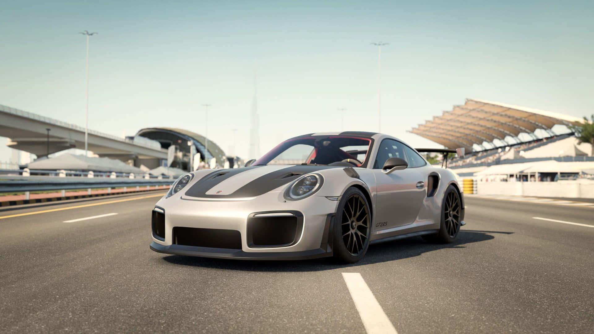 電玩遊戲 桌布 壁紙 — 一輛銀色保時捷911 GT2 RS帶有黑色賽車條紋，在晴朗藍天下，於未來主義體育場附近的現代高速公路上疾馳。
