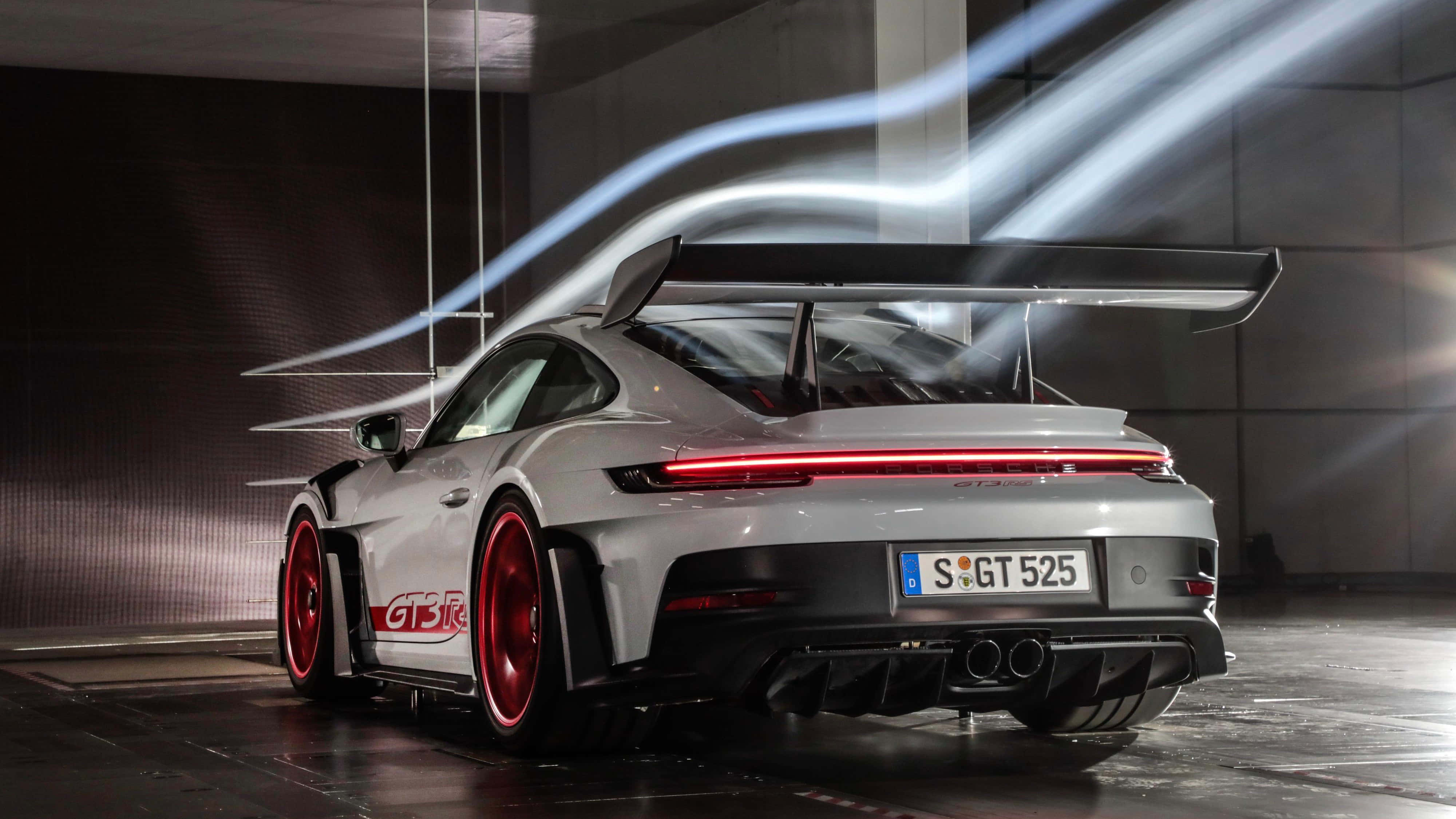 桌布 壁紙 — 一輛銀色保時捷911 GT3 RS，配備紅色輪圈和發光尾燈，在時尚現代車庫內以動態光軌捕捉其行駛姿態。
