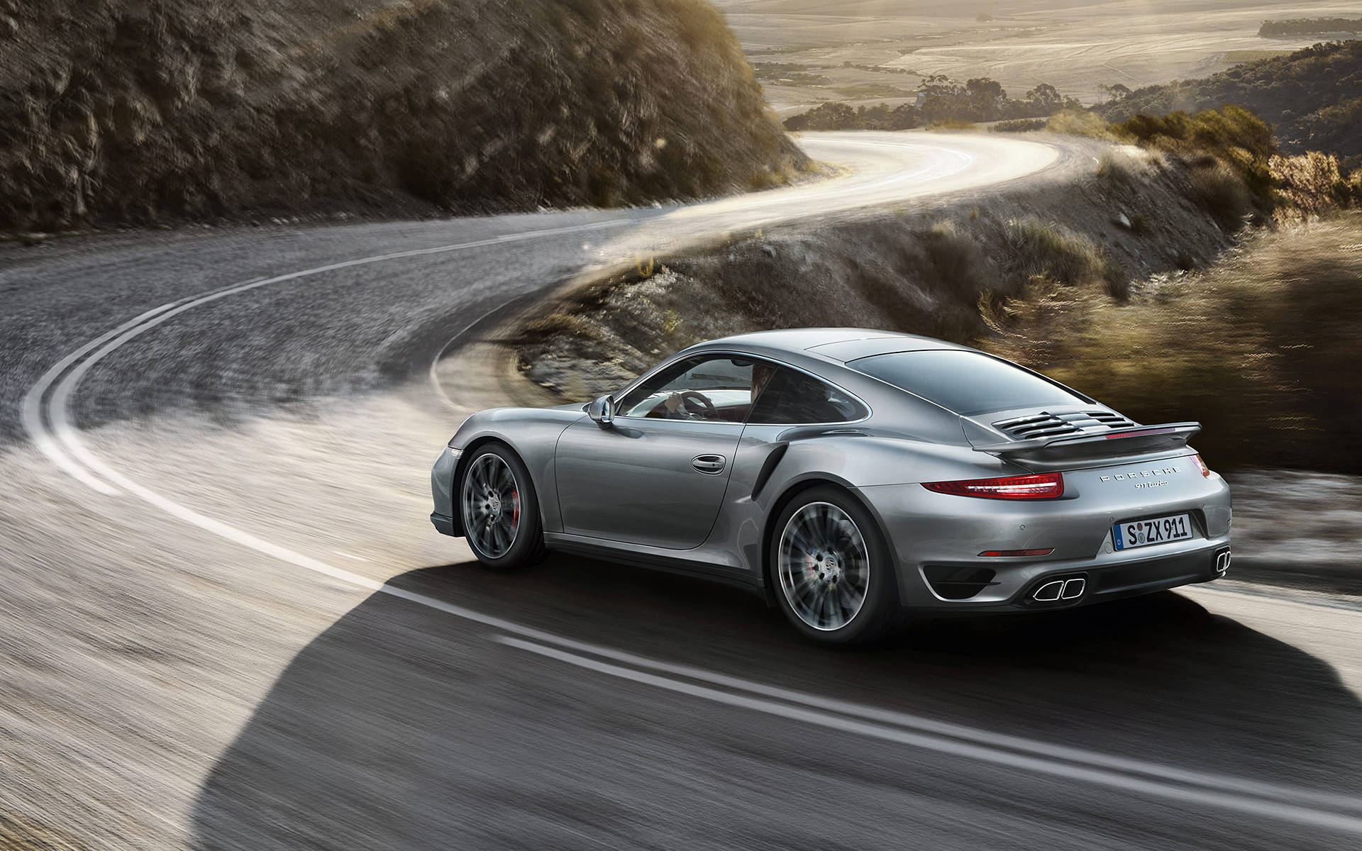 銀色保時捷911 Turbo在日落時分於蜿蜒的海岸公路上疾馳。