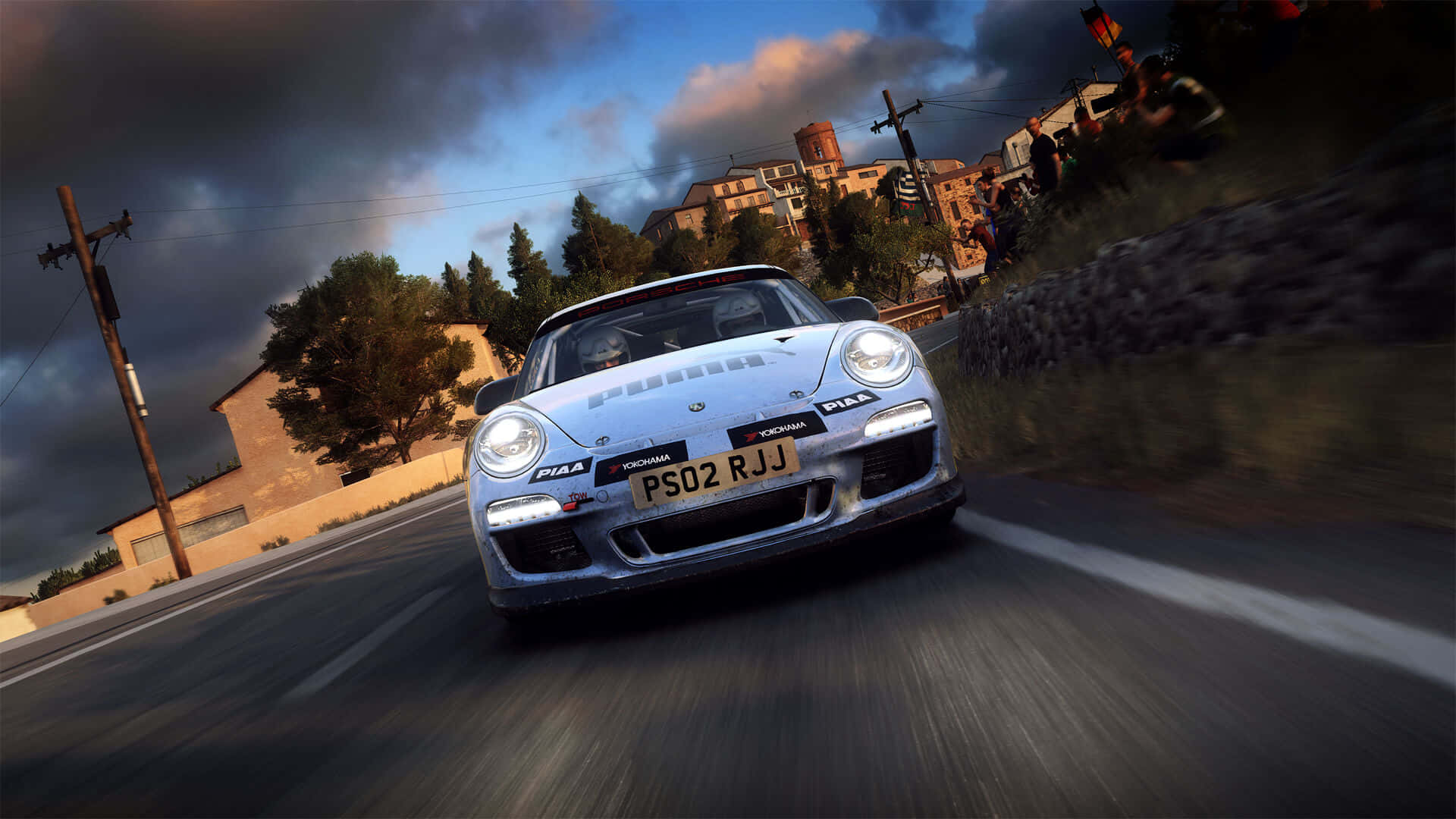 1920x1080 Dirt Rally 桌布 壁紙 — 一輛銀色保時捷911在戲劇性的多雲天空下沿著蜿蜒的鄉村道路奔馳，路邊有觀眾觀看。