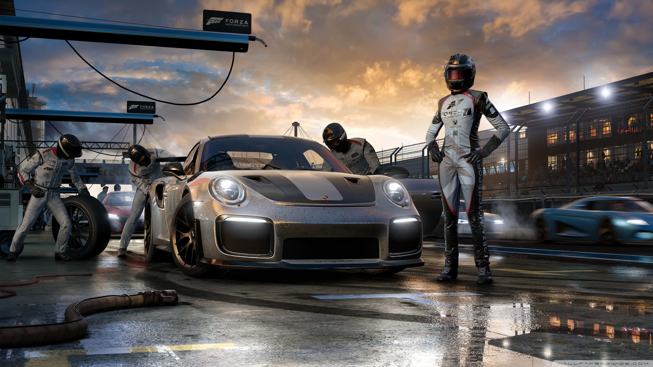 1440p Forza Motorsport 7 桌布 壁紙 — 一輛銀色保時捷賽車在戲劇性的日落中閃耀，維修站工作人員在潮濕的賽道上迅速工作。