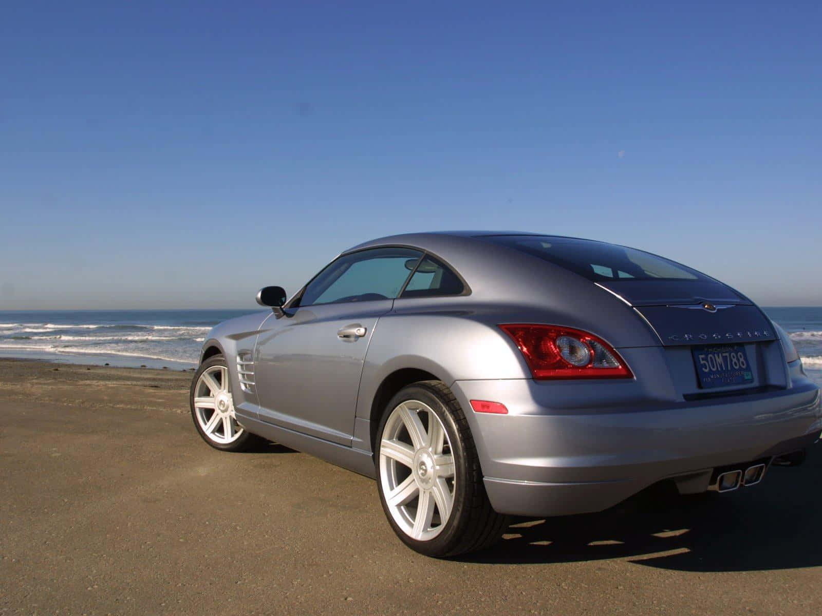 Chrysler Crossfire 桌布 壁紙 — 一輛銀色克萊斯勒Crossfire跑車停泊在沙灘上，背景有海浪和清澈的藍天。
