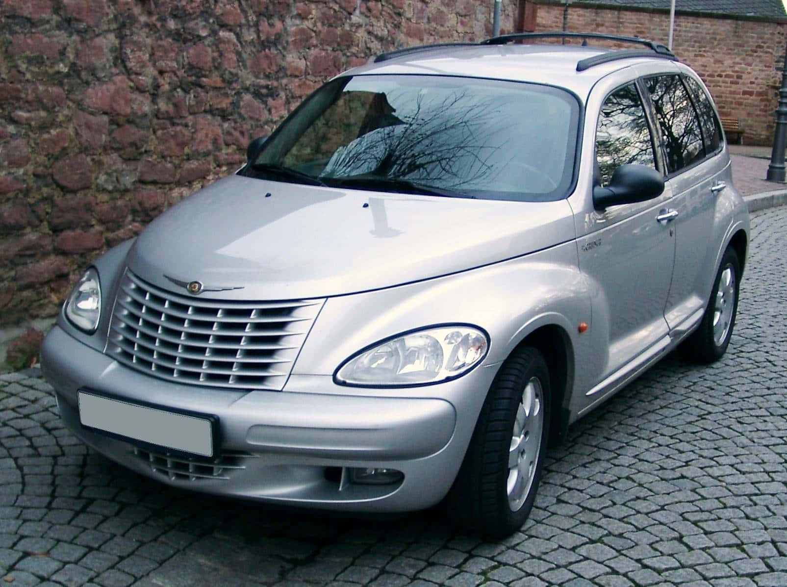 Chrysler Pt Cruiser 桌布 壁紙 — 一輛銀色克萊斯勒PT Cruiser停放在紅磚牆旁的鵝卵石街道上。