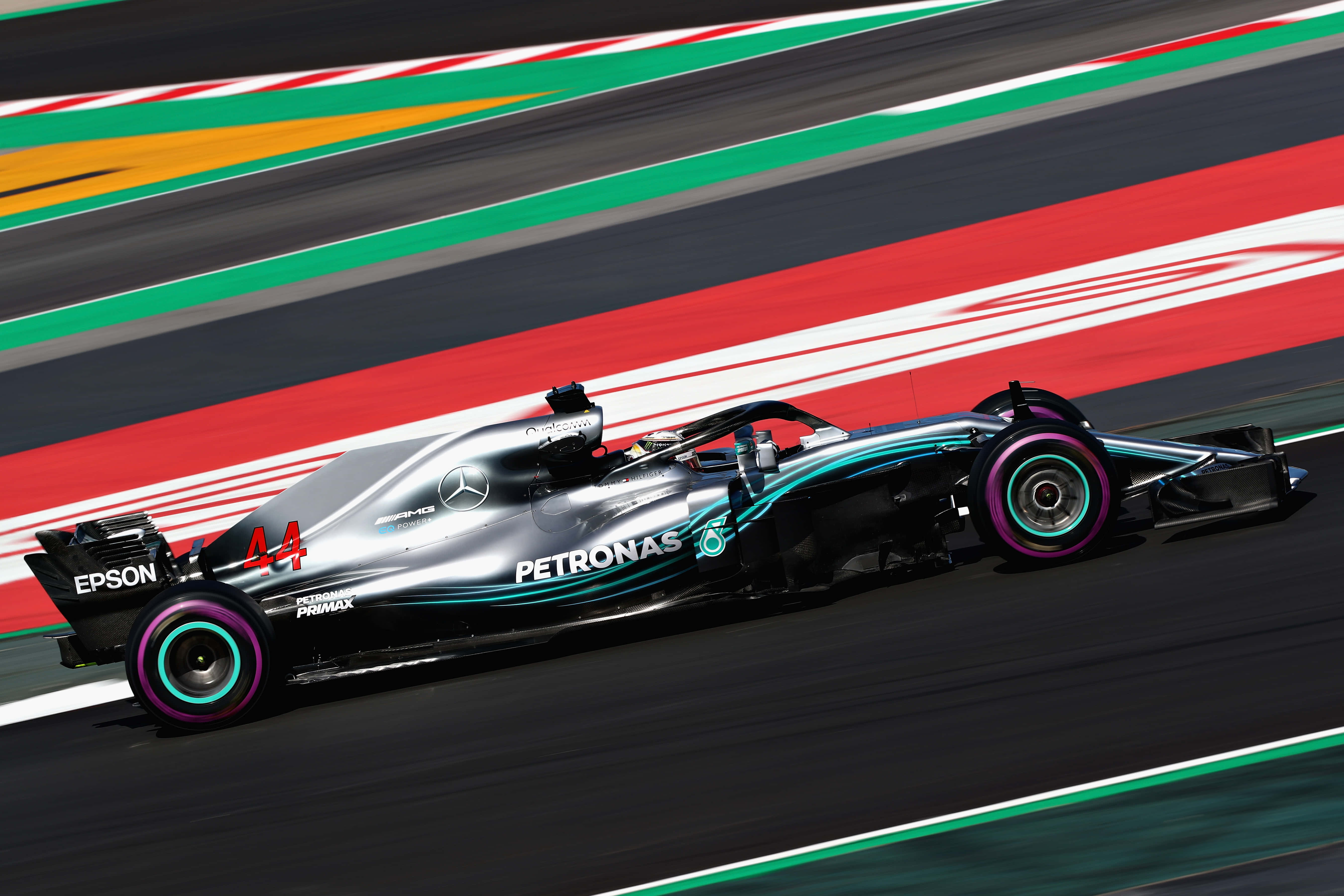 Mercedes 桌布 壁紙 — 一輛銀色和藍綠色的 Formula 1 賽車，編號 44，在帶有紅色、綠色和白色路緣的賽道上高速奔馳。
