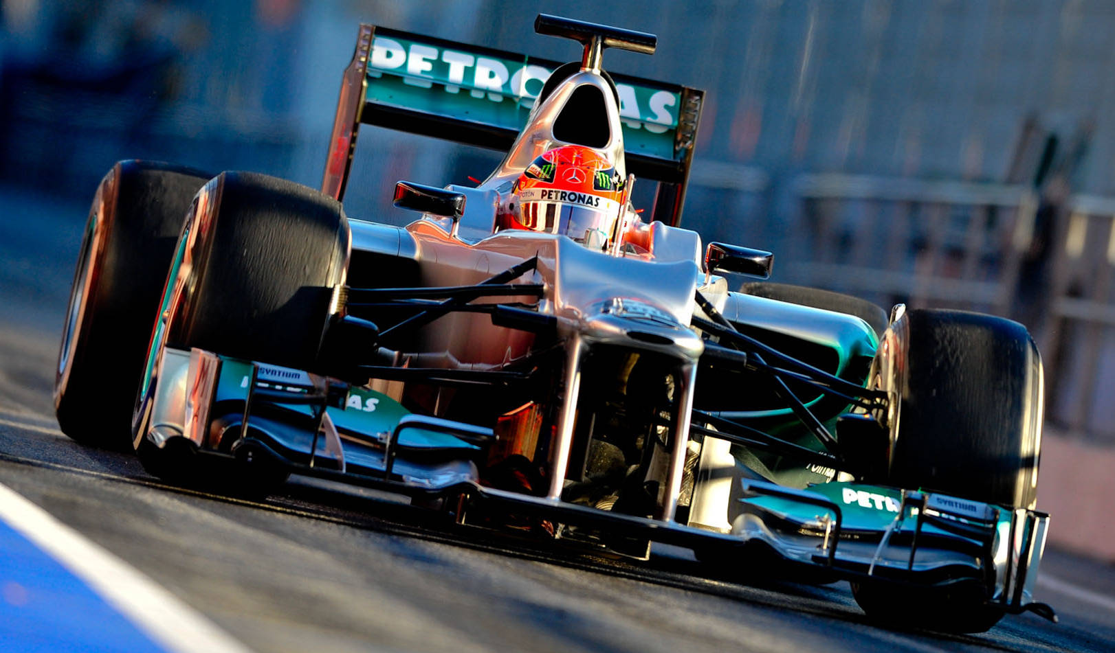 michael 桌布 壁紙 — 一輛銀色和藍綠色的F1賽車帶有Petronas品牌標誌，在明亮的日光下沿著賽道飛馳。