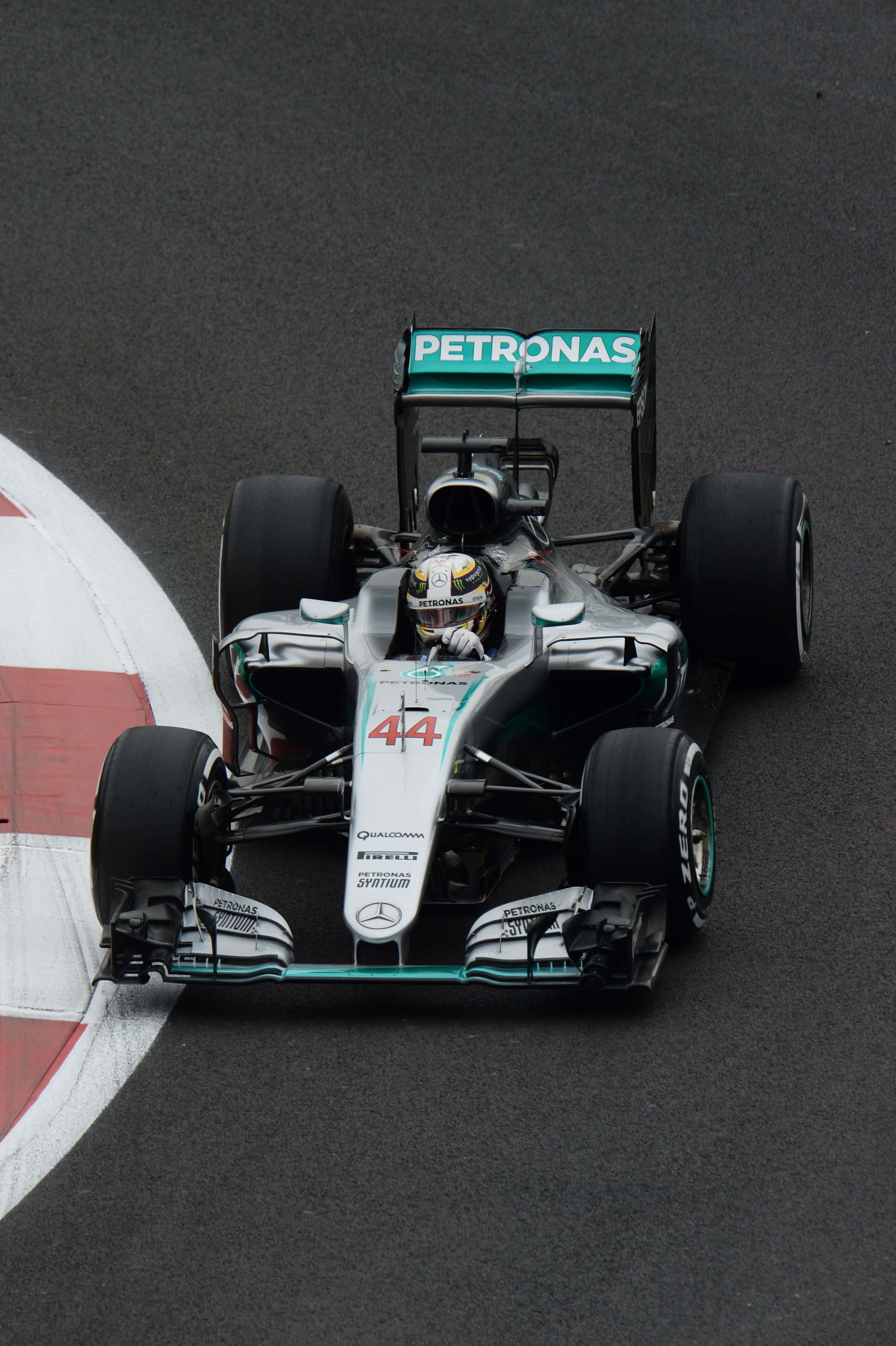 F1 2016 桌布 壁紙 — 一輛銀色和藍綠色的梅賽德斯一級方程式賽車，編號44，在濕滑的瀝青賽道上繞過紅白路緣石奔馳。