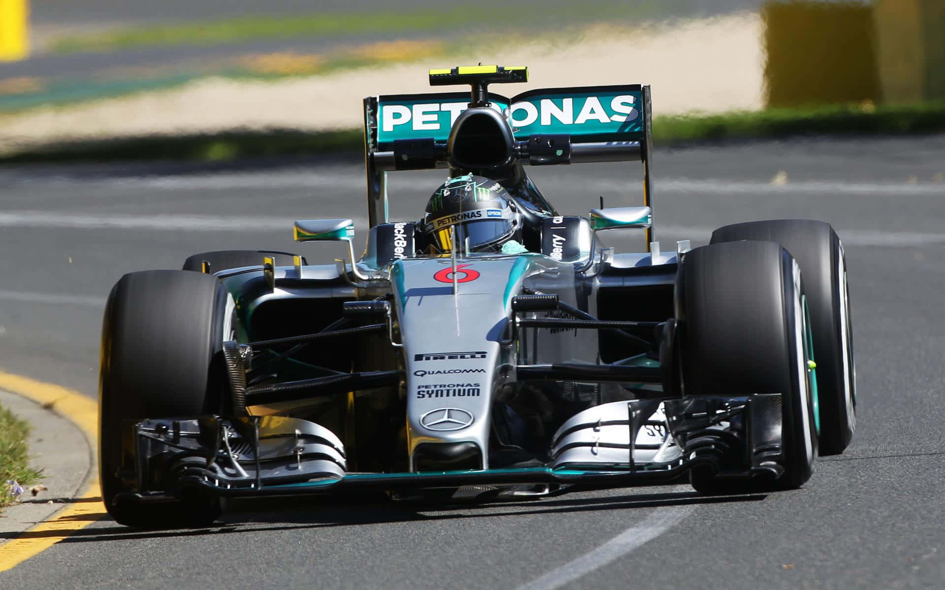 F1 2016 桌布 壁紙 — 一輛銀色和藍綠色的賓士一級方程式賽車在賽道彎道高速行駛，車手戴著頭盔清晰可見。