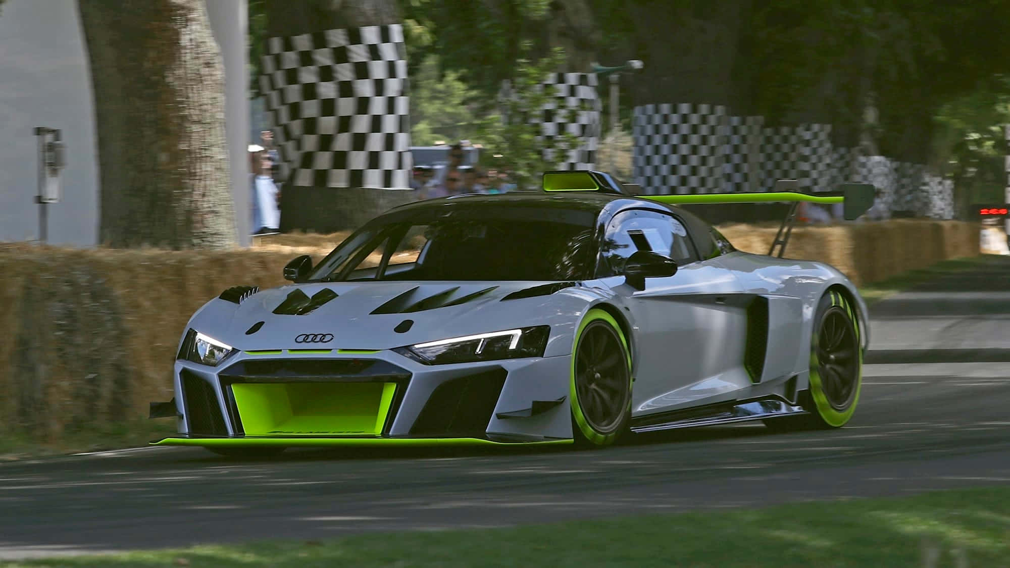 奧迪 桌布 壁紙 — 一輛銀色奧迪R8 LMS GT3賽車帶有螢光綠色點綴，在陽光明媚的賽道上飛馳而過乾草捆和方格旗。