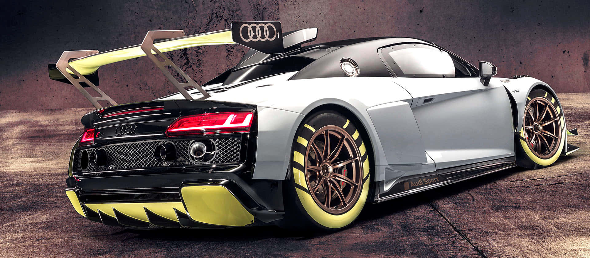 奧迪 桌布 壁紙 — 一輛銀色奧迪R8 LMS GT3賽車，帶有黃色點綴和大型尾翼，停在混凝土表面上。