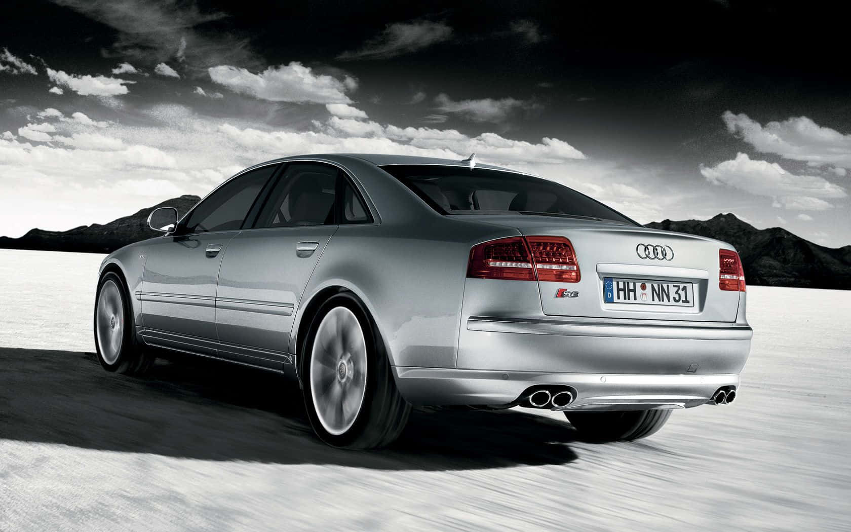 Audi S8 桌布 壁紙 — 一輛銀色奧迪S8轎車在戲劇性的多雲天空下，越過雪原，遠處有山巒。