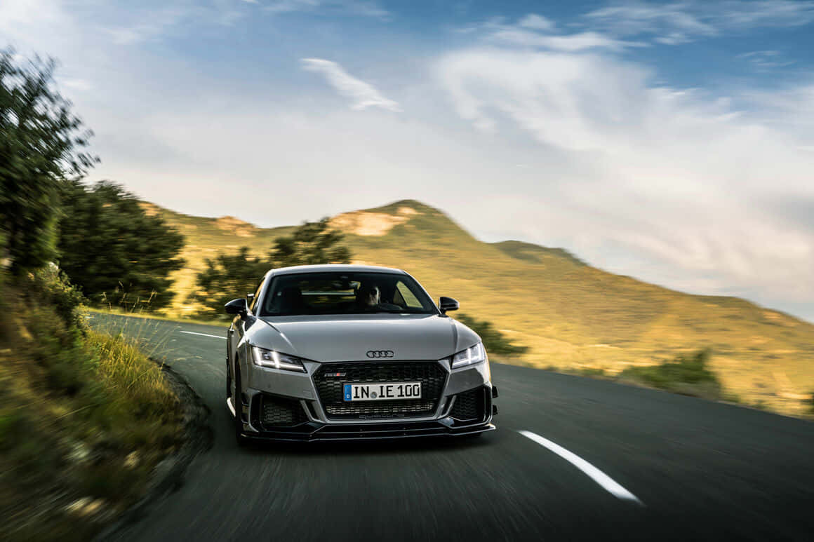 Audi Tt Rs 桌布 壁紙 — 一輛銀色奧迪TT RS在晴朗藍天白雲下，沿蜿蜒山路飛馳。