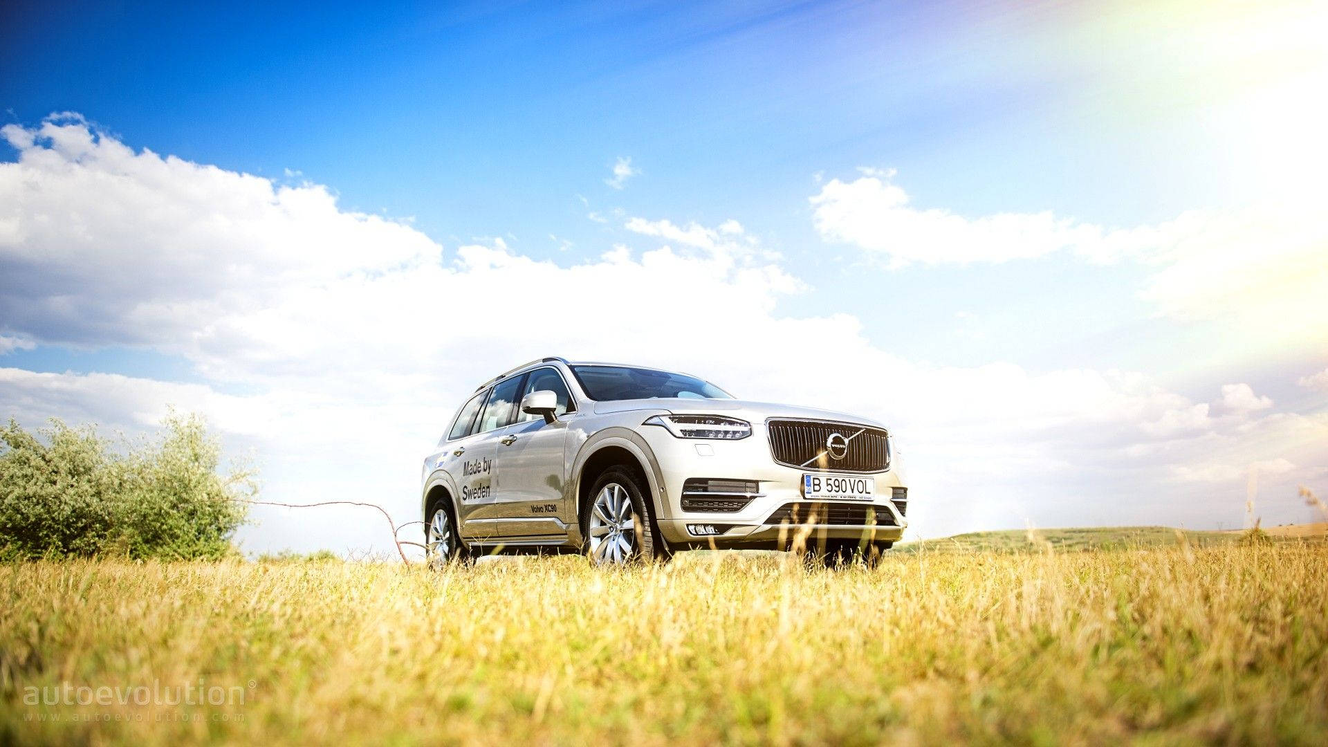 Volvo 桌布 壁紙 — 一輛銀色富豪SUV停泊在金色草地上，背景是明亮的藍天和蓬鬆的白雲。