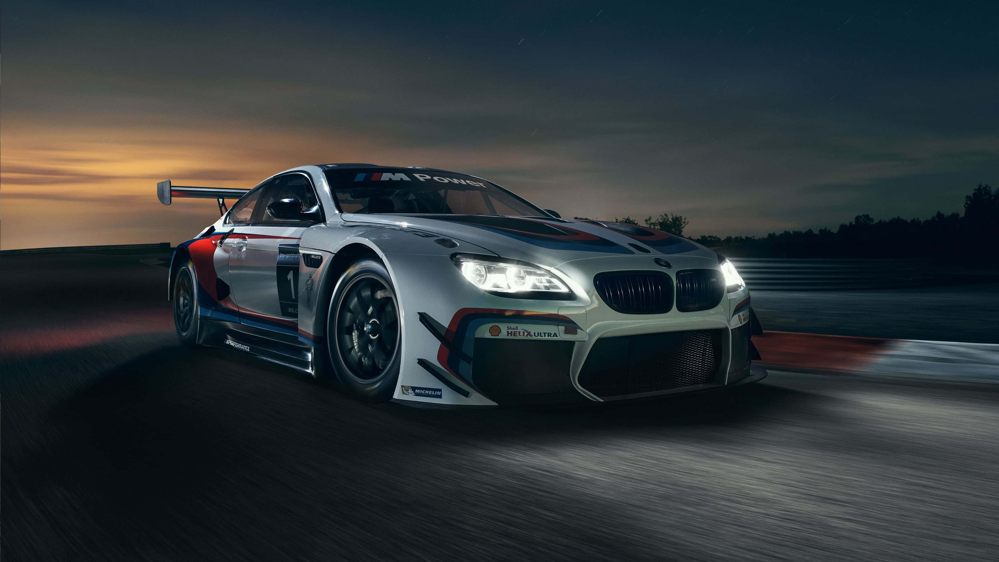 Bmw M Series 桌布 壁紙 — 一輛銀色寶馬賽車在黃昏時分在潮濕的賽道上疾馳，車頭燈閃爍，動作模糊。