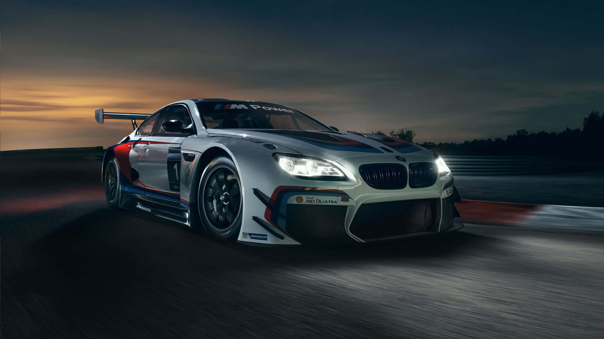 BMW 動圖 桌布 壁紙 — 一輛銀色寶馬賽車在黃昏時分在賽道上疾馳，車頭燈閃爍，帶有動態模糊效果。