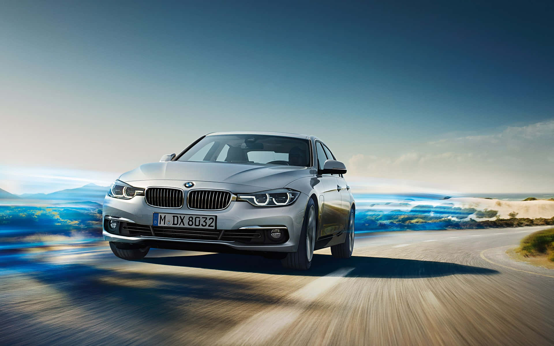 Bmw 328 桌布 壁紙 — 一輛銀色寶馬轎車沿著海岸公路高速行駛，在藍天和海洋背景下呈現模糊的動態效果。