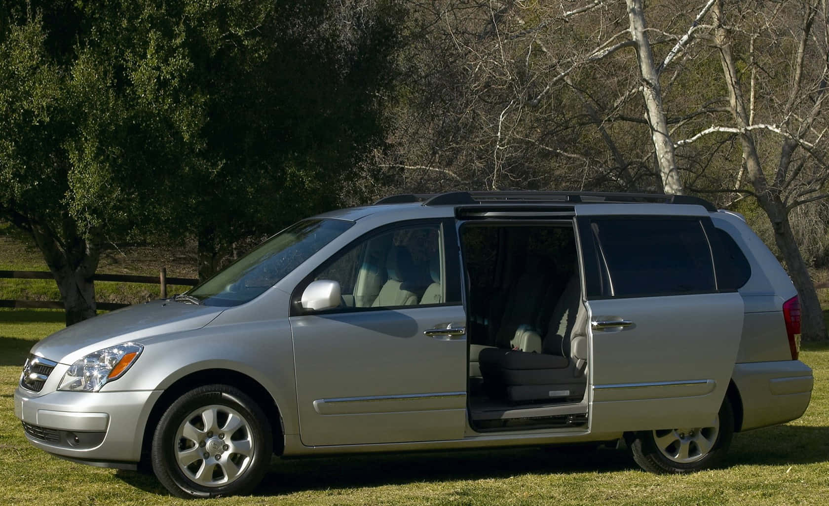 Hyundai Entourage 桌布 壁紙 — 一輛銀色小型貨車停在草地上，側門打開，露出被樹木環繞的內部座椅。