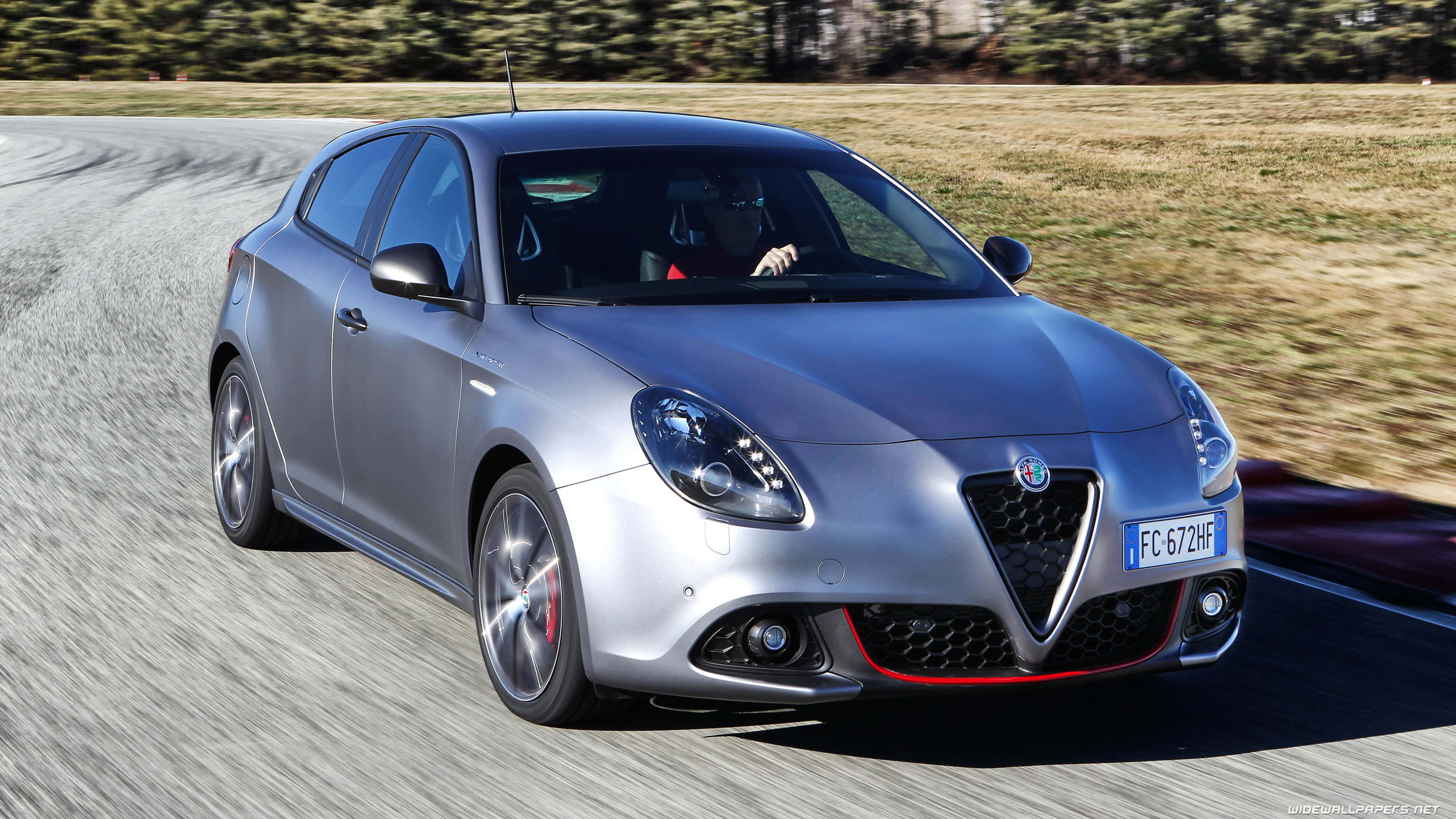 Alfa Romeo Giulietta 桌布 壁紙 — 一輛銀色愛快羅密歐Giulietta跑車在蜿蜒的道路上奔馳，背景是模糊的草地。