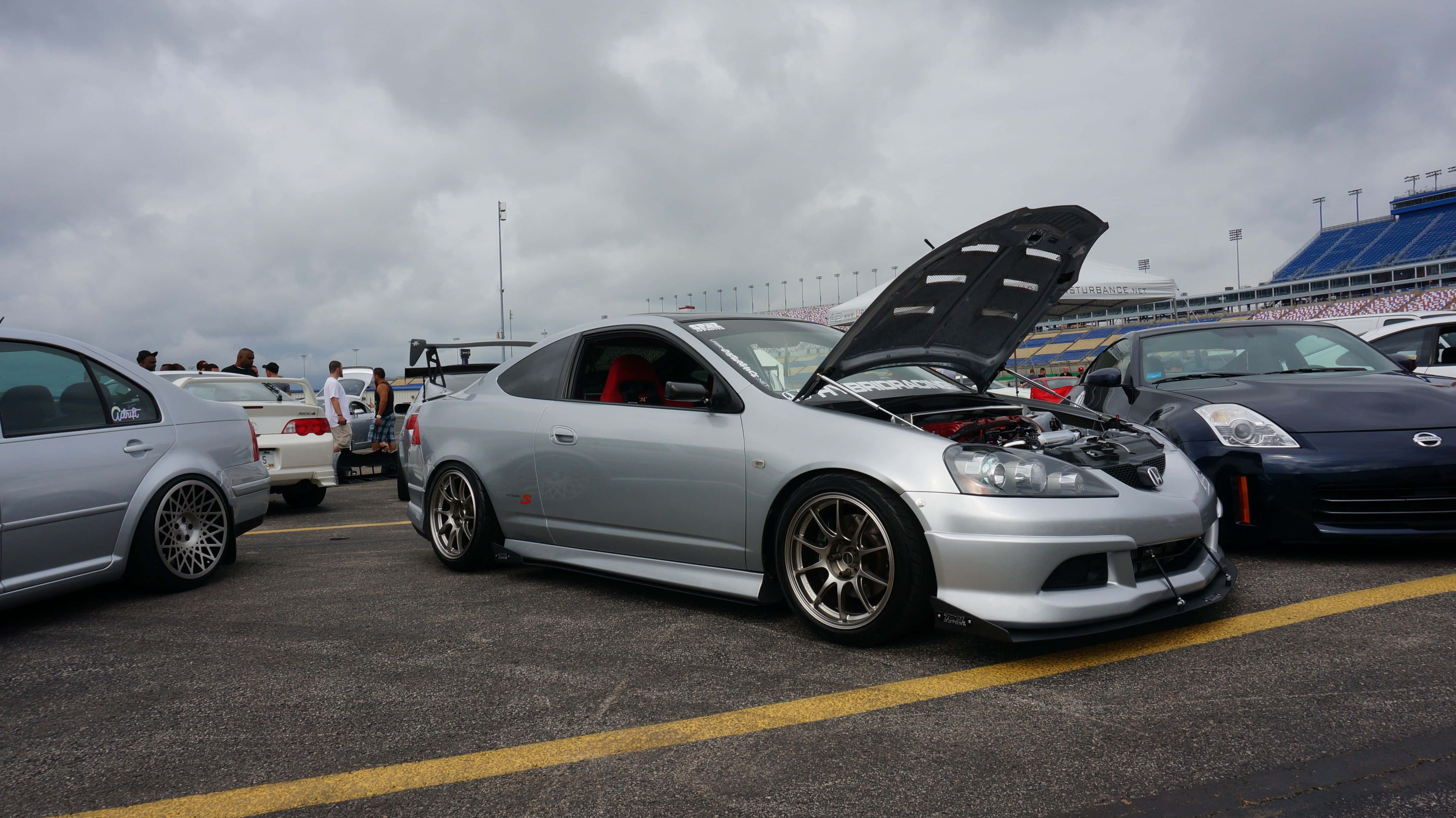 Rsx Type-s 桌布 壁紙 — 一輛銀色改裝跑車打開引擎蓋，在陰天下的賽車場停車場展示定製引擎。