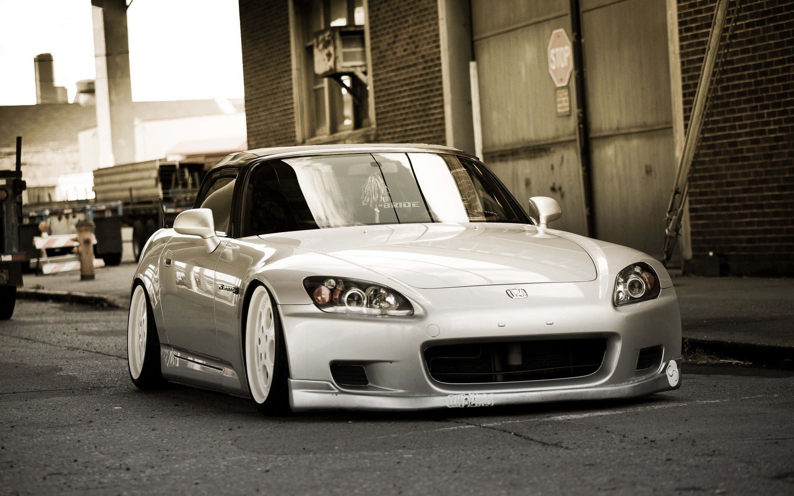 Honda S2000 桌布 壁紙 — 一輛銀色改裝跑車配白色輪胎，停放在城市小巷中，溫暖的棕褐色燈光下。