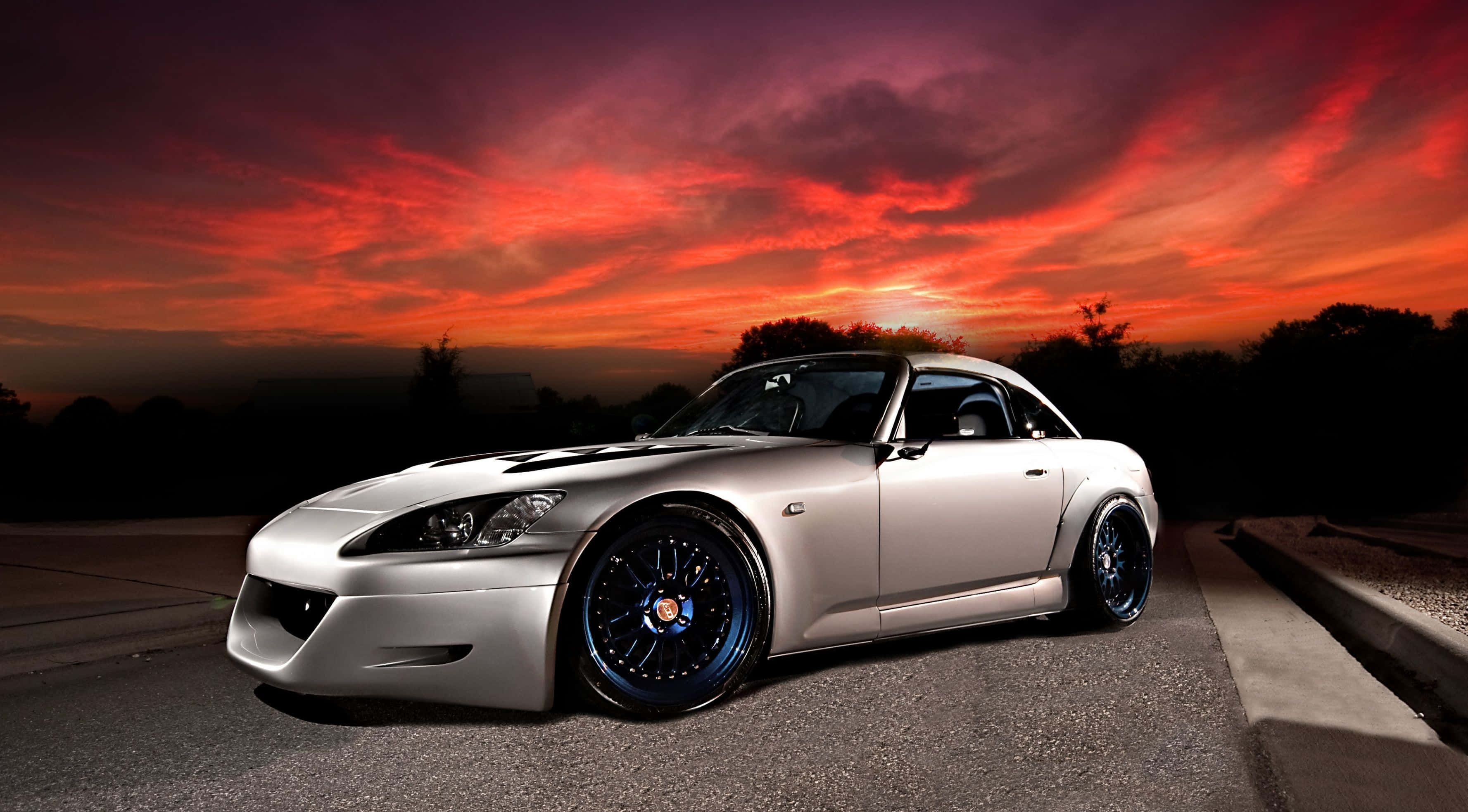 Honda S2000 桌布 壁紙 — 一輛銀色改裝跑車配藍色輪圈，停在瀝青路面上，背景是火紅與紫色的日落天空。