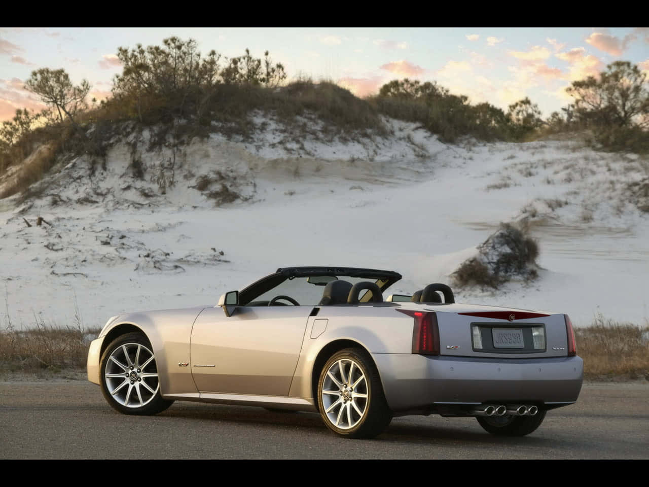 Cadillac Xlr 桌布 壁紙 — 一輛銀色敞篷跑車停在日落時分雪覆沙丘旁的道路上。